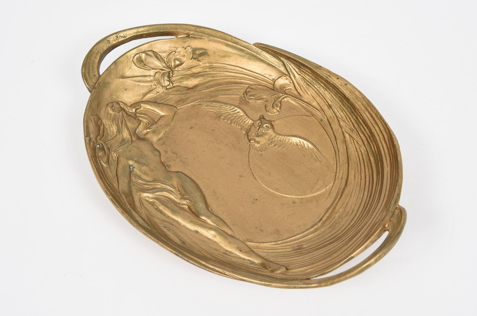 Art Nouveau dore bronze tray features a figural motif in semi-relief, depicting a sensuous maiden figure surrounded by iris flowers, with a flying owl and a moon in the background. The flowing lines and naturalistic forms are characteristic of the