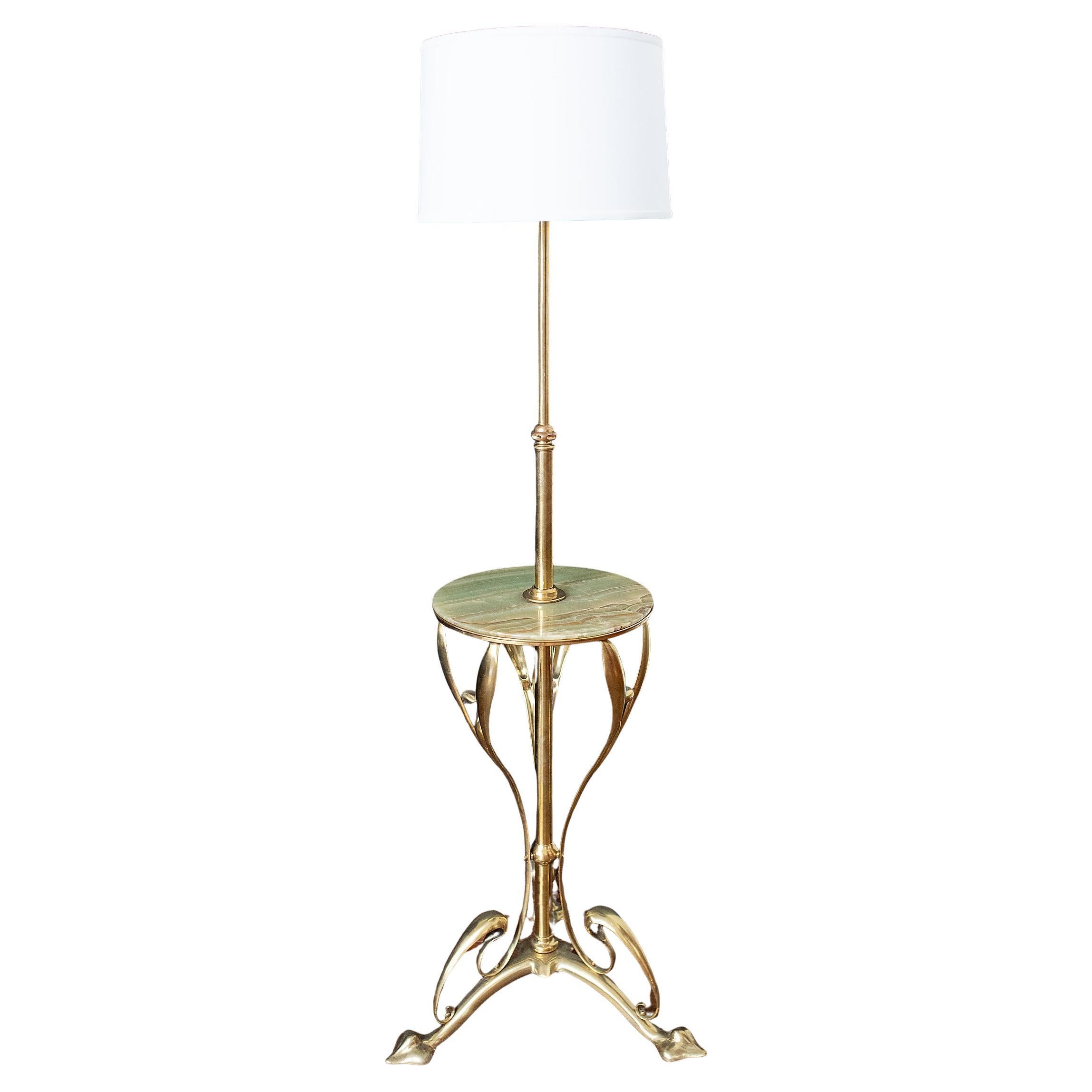A fine French standing floor lamp of brass and green onyx marble from the Art Nouveau period, featuring a brass column and ornate scrolling supports at the base and beneath the tabletop, the base resting on three pad feet. 

A circular, light green