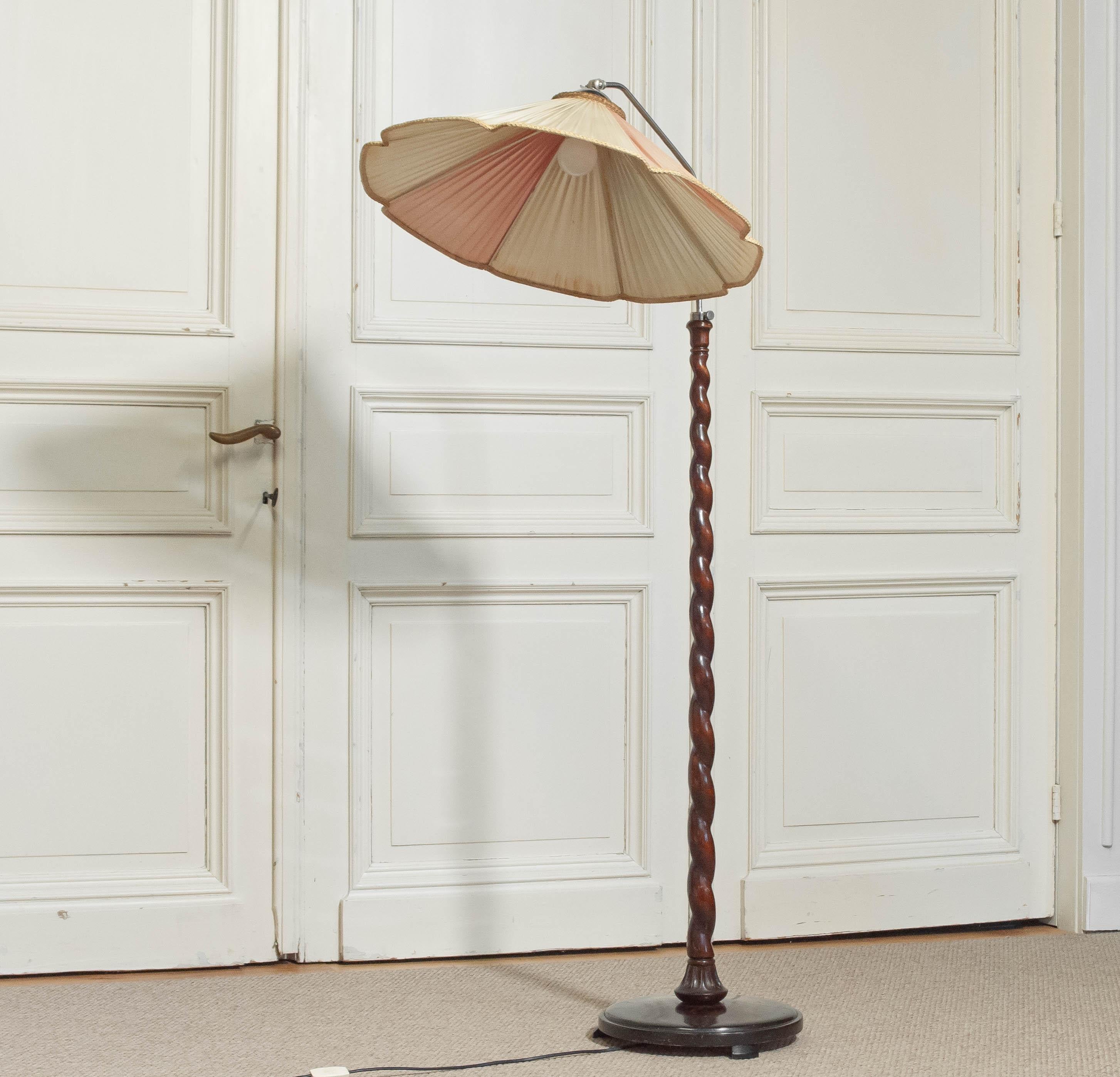 Elegant 1940s floor lamp featuring a beautifully hand-carved twisted wooden stem and a large original pleated fabric shade in warm tones. The shade is adjustable and can be tilted to direct light as needed, making it both decorative and