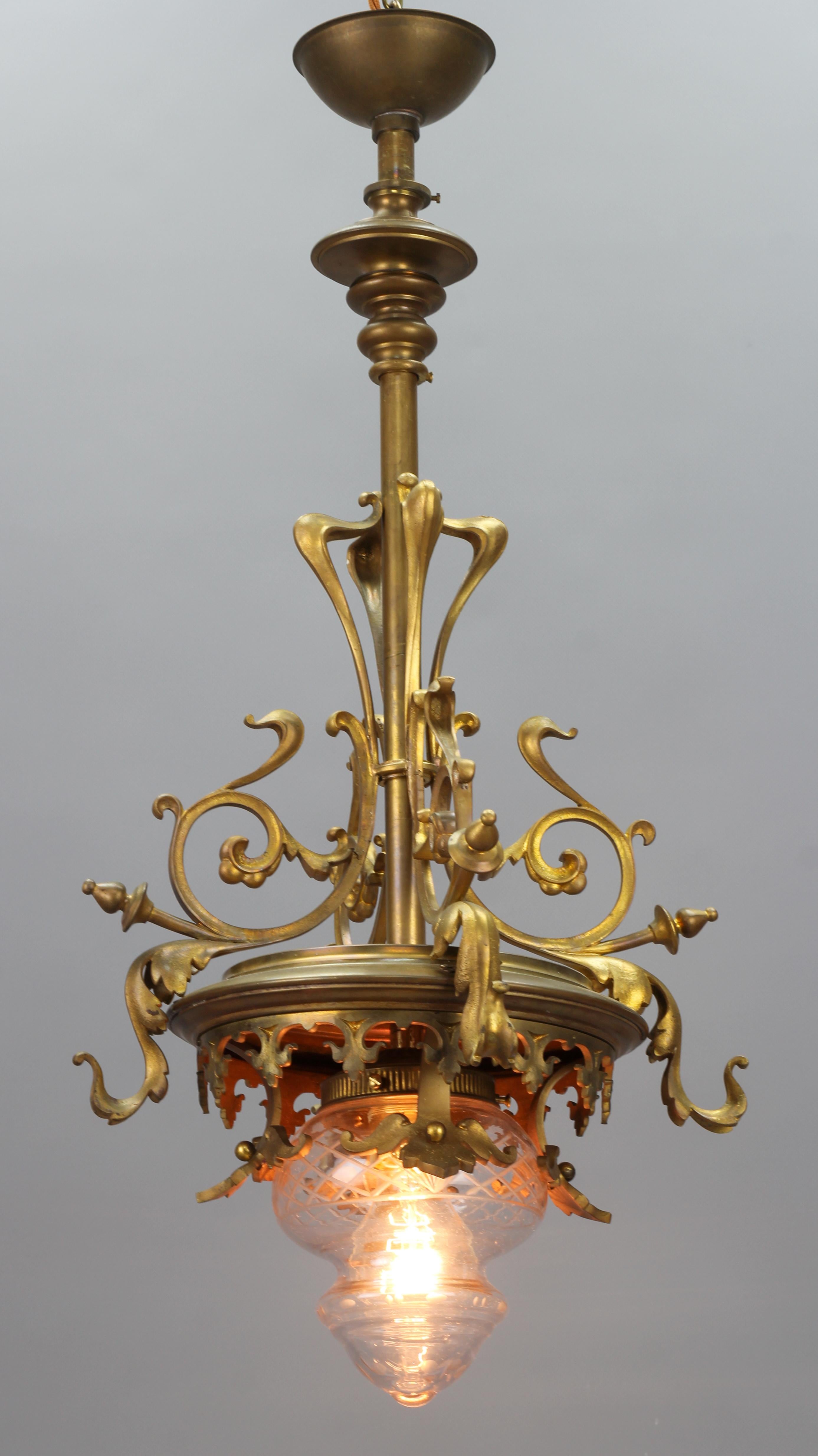 Art Nouveau French brass and cut glass pendant chandelier from the 1920s.
This beautiful and ornate brass pendant light fixture features characteristic Art Nouveau period brass decors and an unusual shape clear, cut glass lamp shade.
One socket for