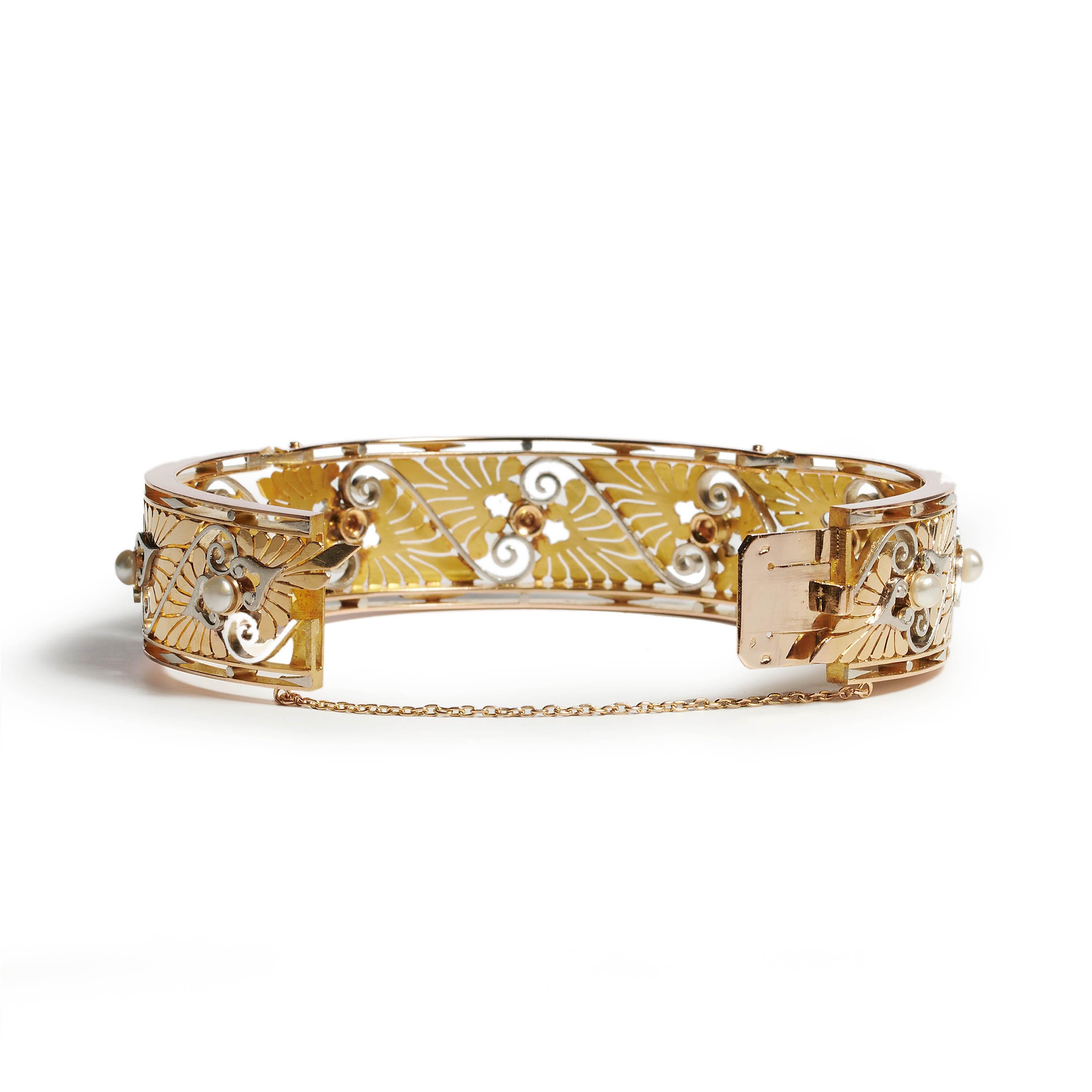 A French, Art Nouveau, pearl gold and platinum bangle, with a repeat pattern of bouton pearls, individually set between motifs of opposing gold acanthus leaves, divided by platinum scrolls, bordered by knife edges, with dot and lozenge infilled