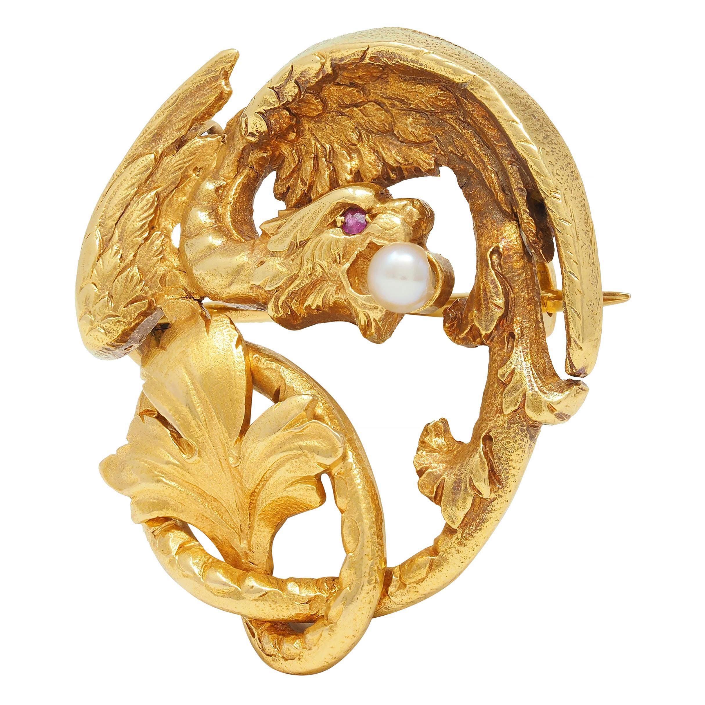 Designed as a highly rendered stylized depiction of a griffin winding in a circle 
With lion head, wings, and knotted foliate tail - engraved with texture
Featuring a 3.0 mm round pearl clutched in its mouth 
Cream in body color with strong