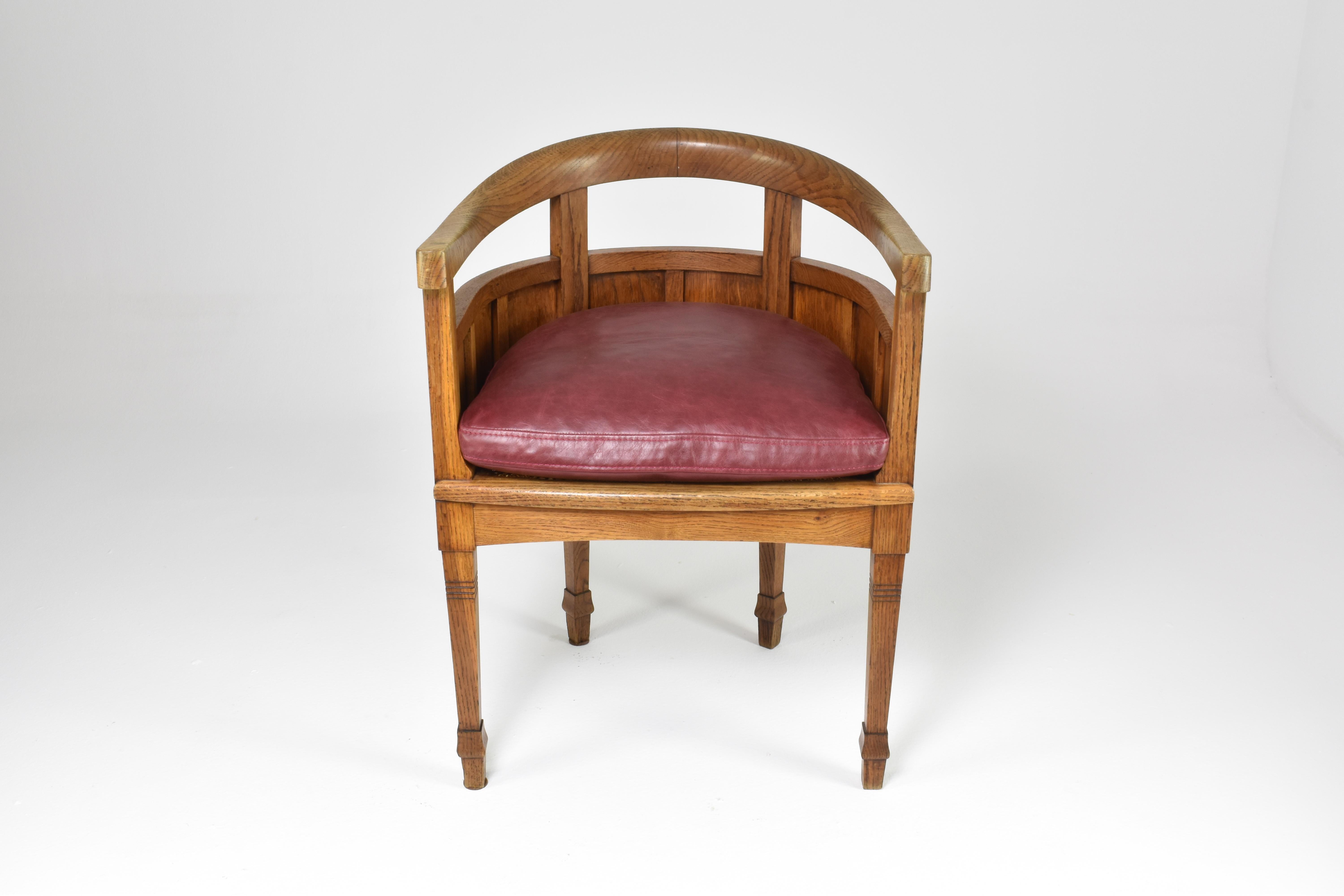 An exquisite office chair fashioned from solid oak wood dating back to the 1920s. The chair's seat was masterfully reupholstered in a rich, dark red vegetable-tanned leather. The piece boast intricately carved wooden accents throughout. The rounded
