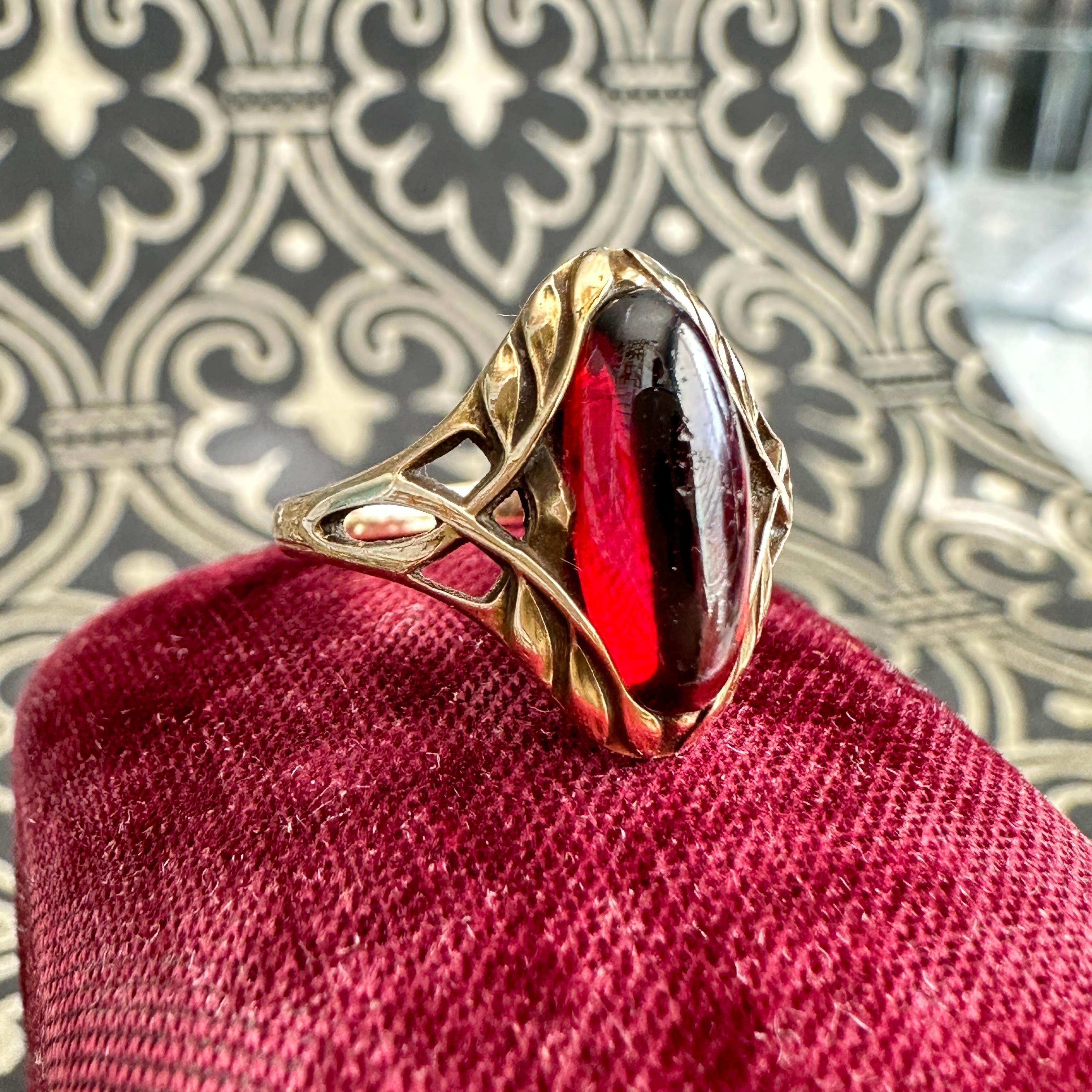 Details: 
Fabulous Art Nouveau Garnet ring, set in 14K yellow gold. Sweet and very unique Art Nouveau setting—definitely a rare find! The cabochon deep red garnet measures 12mm x 5mm and has a great glow in the sunlight. The ring sits 4.8mm high.