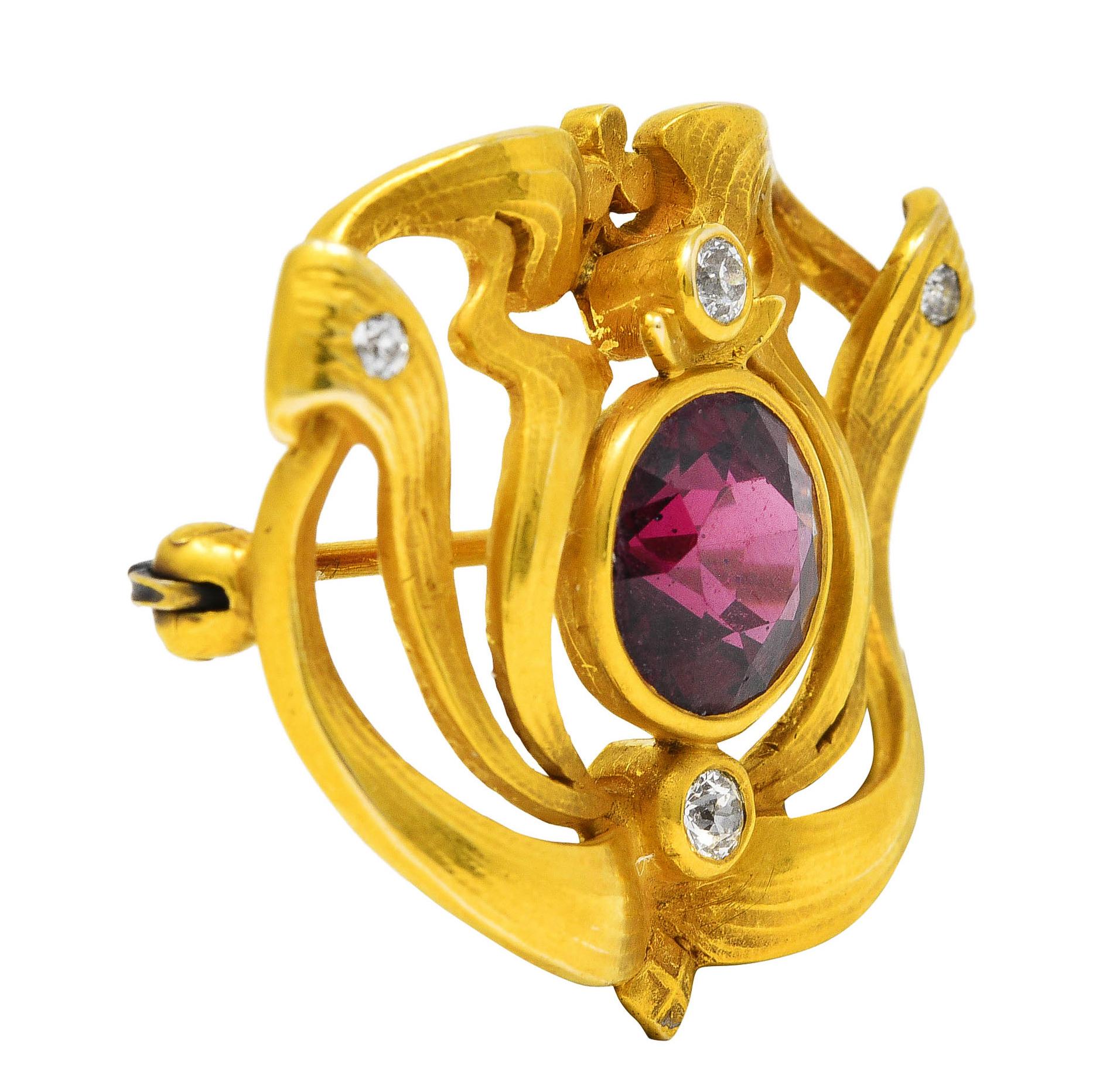 Centering an 8.0 mm round cut garnet - deeply saturated transparent purplish red in color. Bezel set with a billowing gold whiplash motif surround - grooved and finely textured. With old European cut diamonds bezel and flush set throughout. Weighing