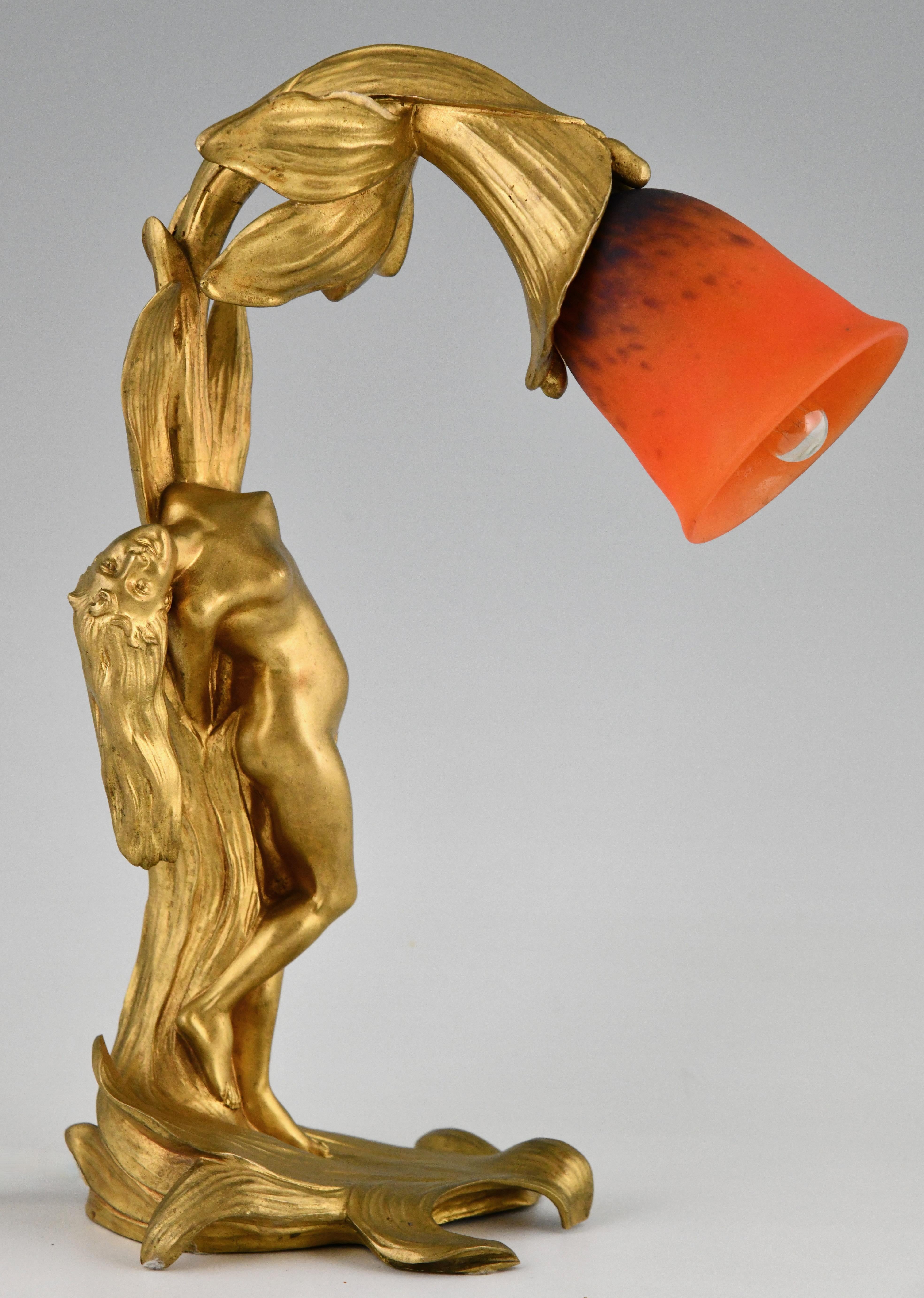 Lámpara Art Nouveau de bronce dorado con desnudo de Helène Sibeud.
Pantalla de cristal firmada Schneider. Francia ca. 1900. 
Pantalla de cristal paté de verre naranja y azul. 
	
Etains 1900, Philippe Dahan. 
Las ediciones del aficionado. 