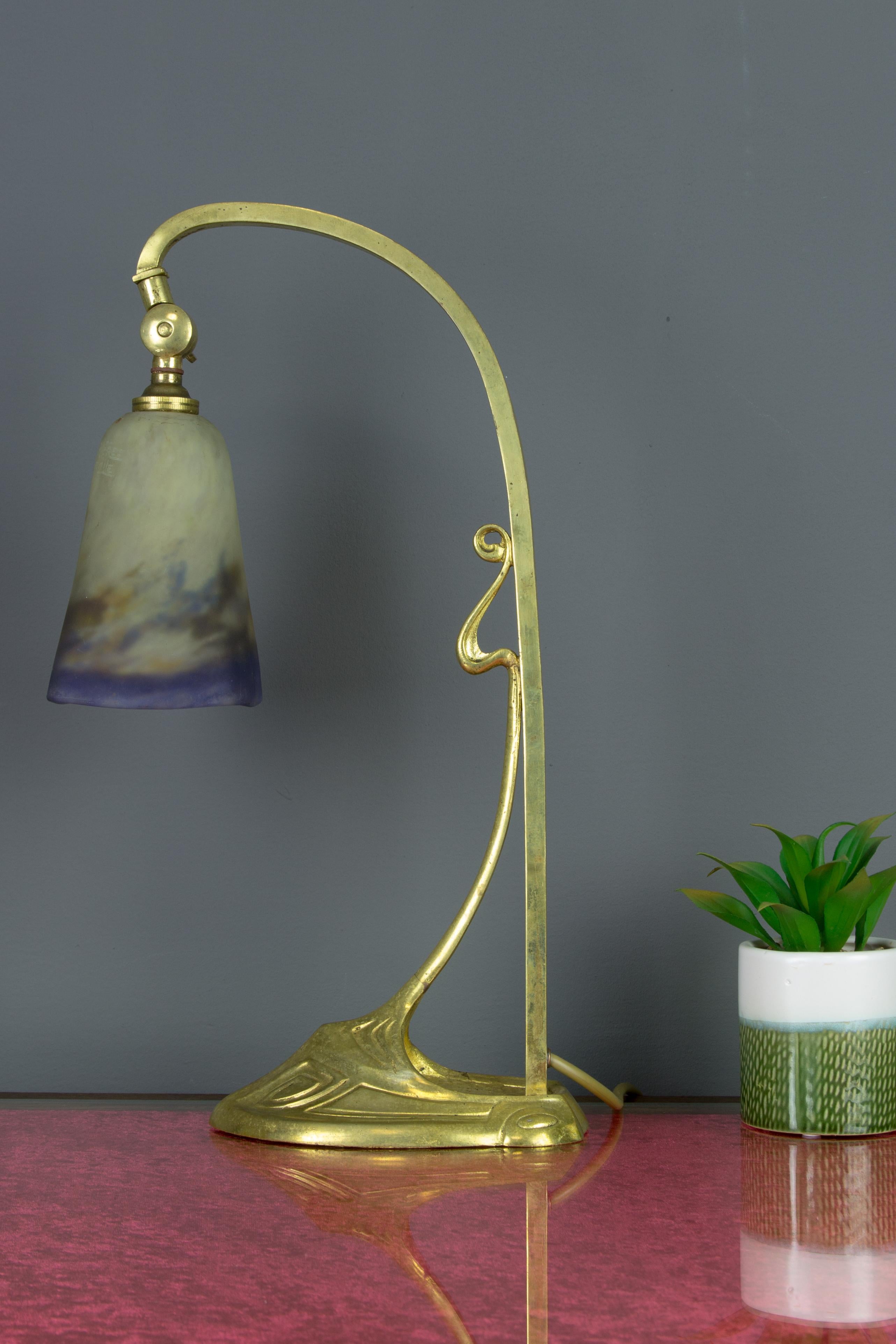 This adorable French Art Nouveau period table lamp features beautiful gilt bronze detailing with typical lines and ornaments of Art Nouveau style. An attractive “pate-de-Verre” lampshade in crème, with blue, purple, green, and brown color accents;