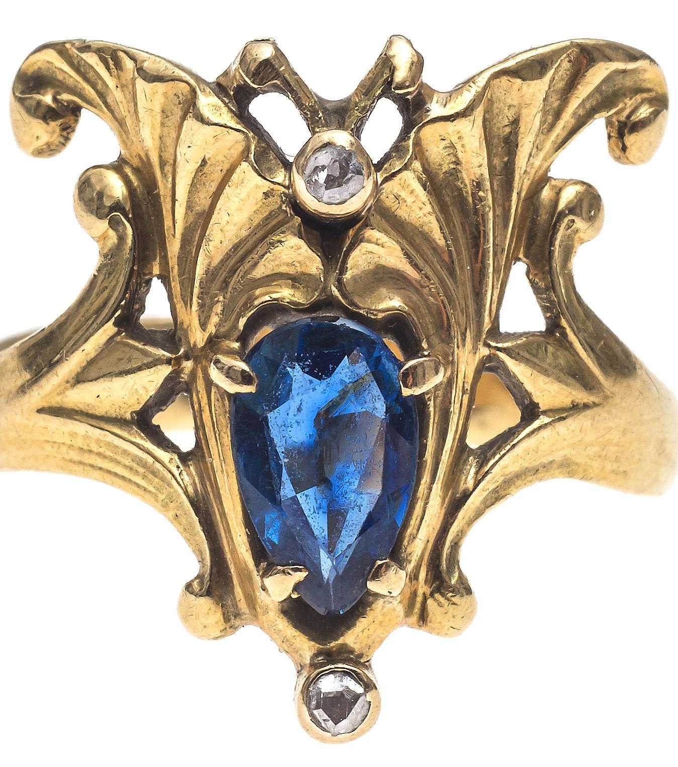 Finely chiselled Art Nouveau ring in 18K gold. The shank terminates in two lotus flowers. The two lotus flowers hold two ginkgo leaves which in turn are holding a drop shaped sapphire. Two small gold mounted rose diamonds decorate the front of the
