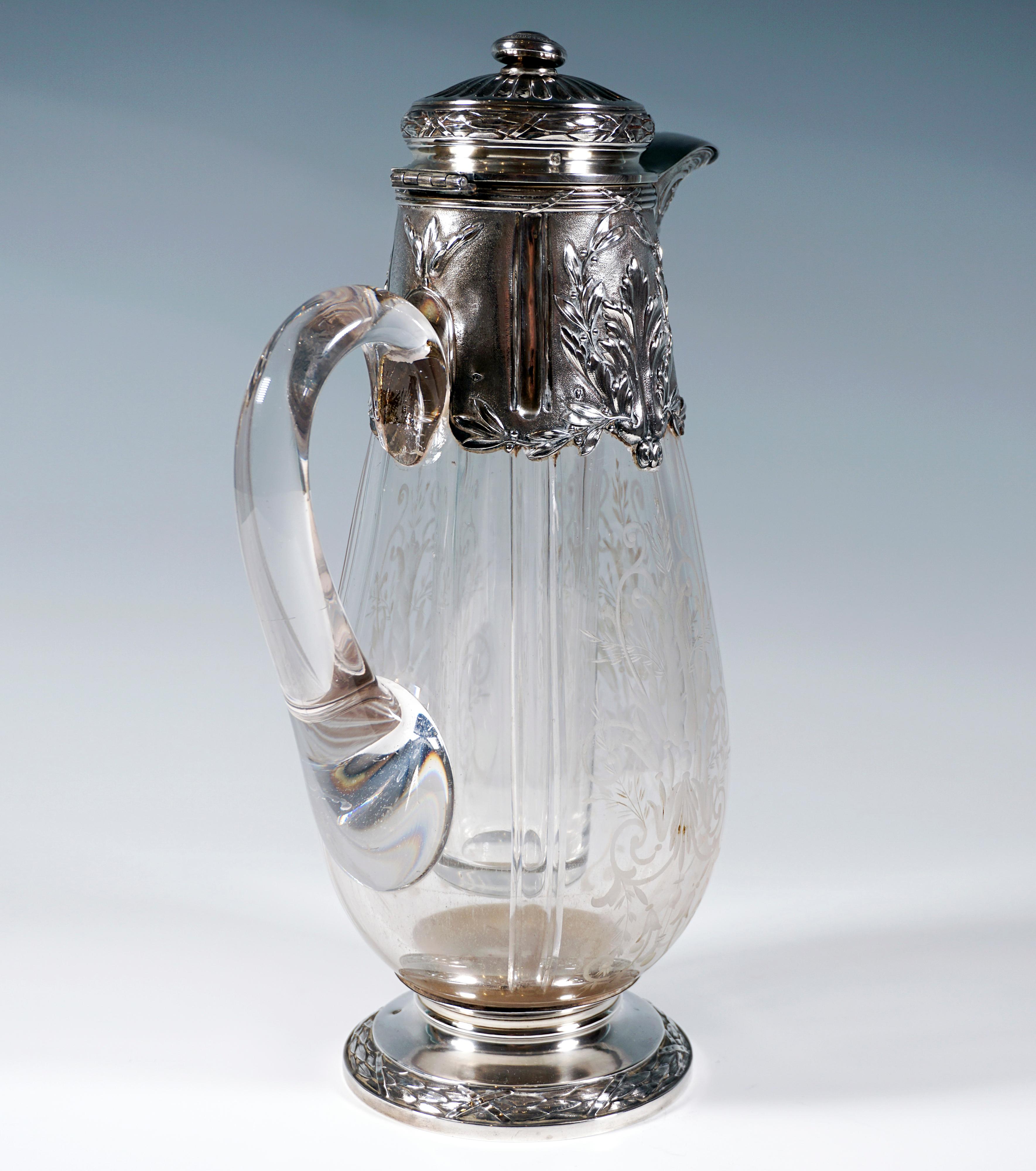 Carafe of clear glass in the form of a drop, the wall divided into four segments by vertical cuts, three segments with elaborately cut floral, foliate and volute bindings, fourth segment with attached, raised handle of glass, foot with mounted,