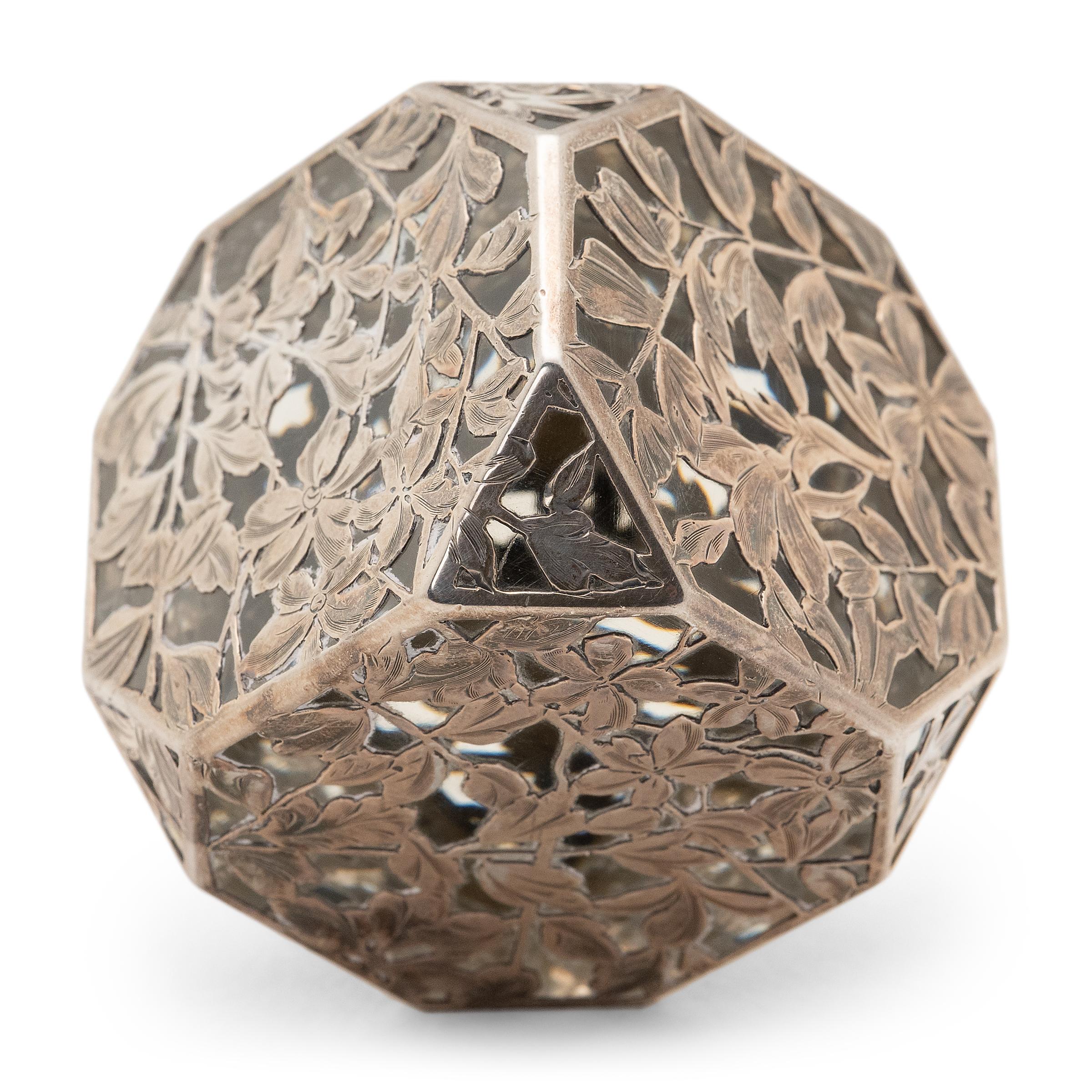This elegant paperweight from the early 20th century is expertly crafted of cut glass and floral silver overlay in the manner of Art Nouveau. The translucent glass cube is shaped with chamfered corners and encased within a silver lattice of flower
