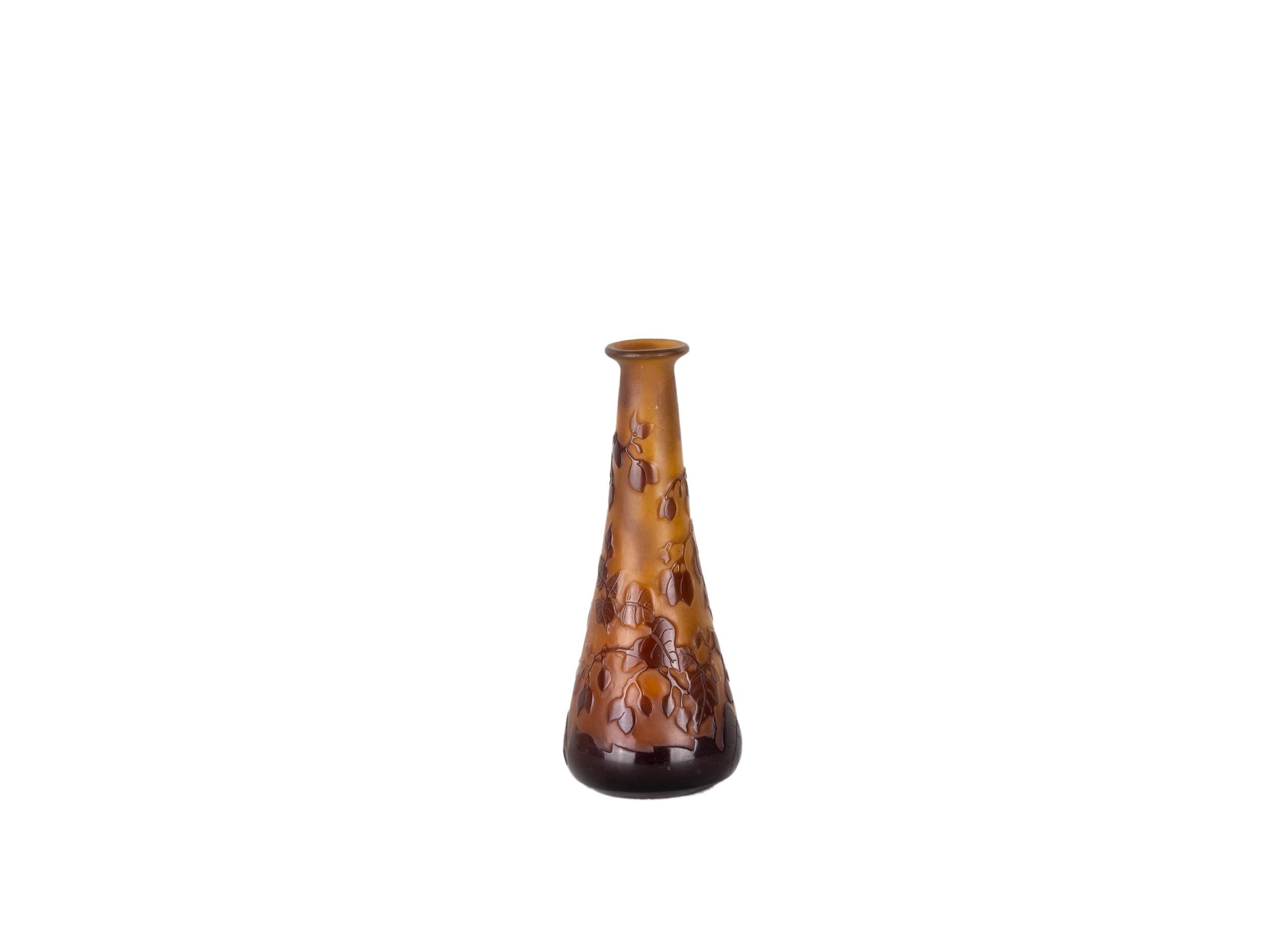 An Art Nouveau glass vase, attributed to Émile Gallé, features a graceful foliage motif in rich amber and brown tones. 
The conical shape enhances the naturalistic relief of leaves and fruit, expertly layered over a translucent base. 
Likely