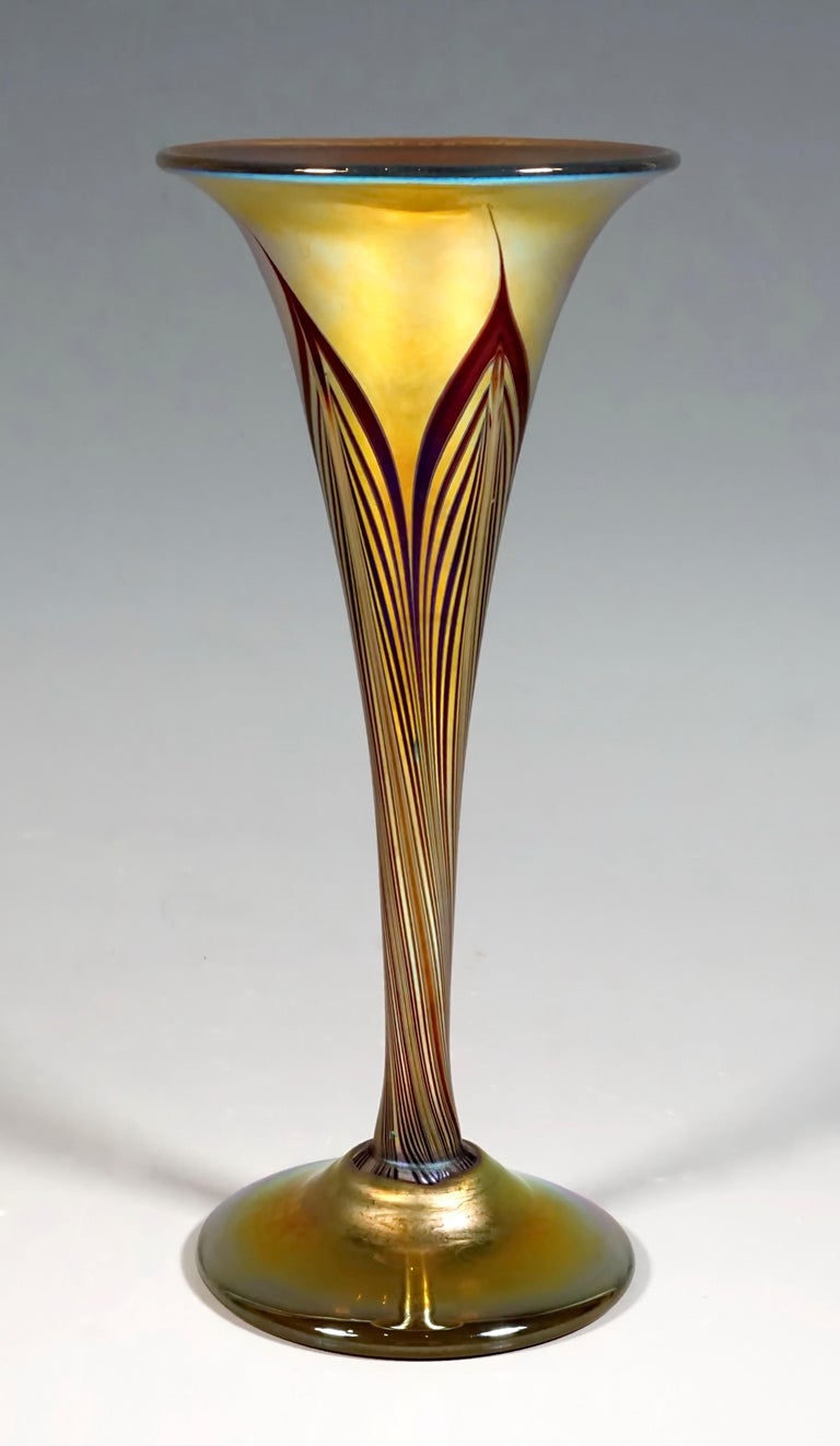 Vase with a funnel-shaped body with a slightly protruding mouth rim, melted on a foot with a slightly arched plate stand, made of so-called favrile glass, colorless glass with yellow and gold-orange-colored melts, iridescent and with combed
