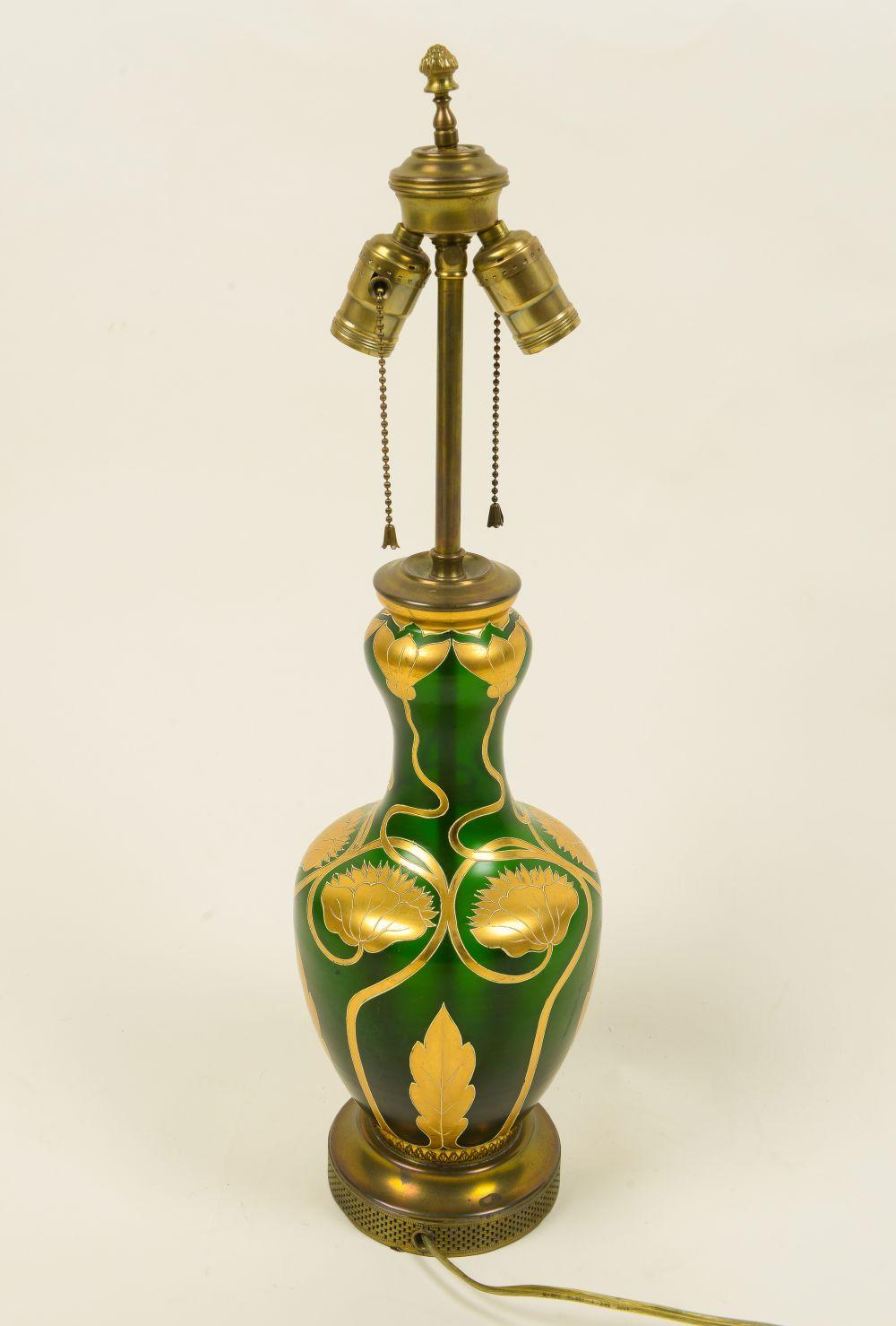 The baluster-form vase decorated overall in gilt with twining vines terminating in peony blossoms with a stiff leaf border at the base; fitted with two bulb sockets; mounted on a brass turned base; adjustable height.
