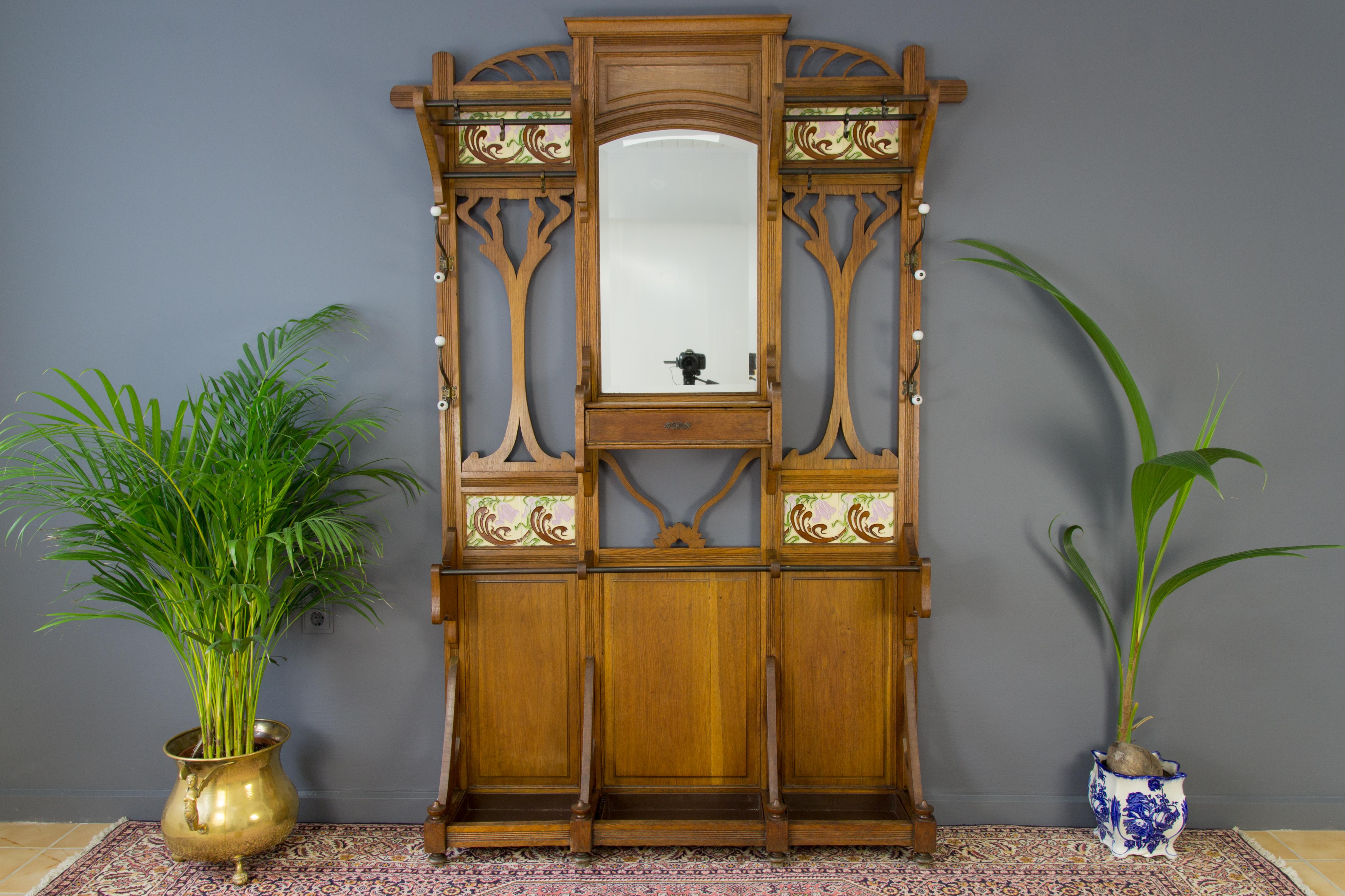 A magnificent French hall stand or hall tree from the Art Nouveau period in the early 1900s has original beveled edge mirror, coat and hat hooks, floral tiles and three drip trays. Beautiful, well-proportioned oak frame in an Art Nouveau typical