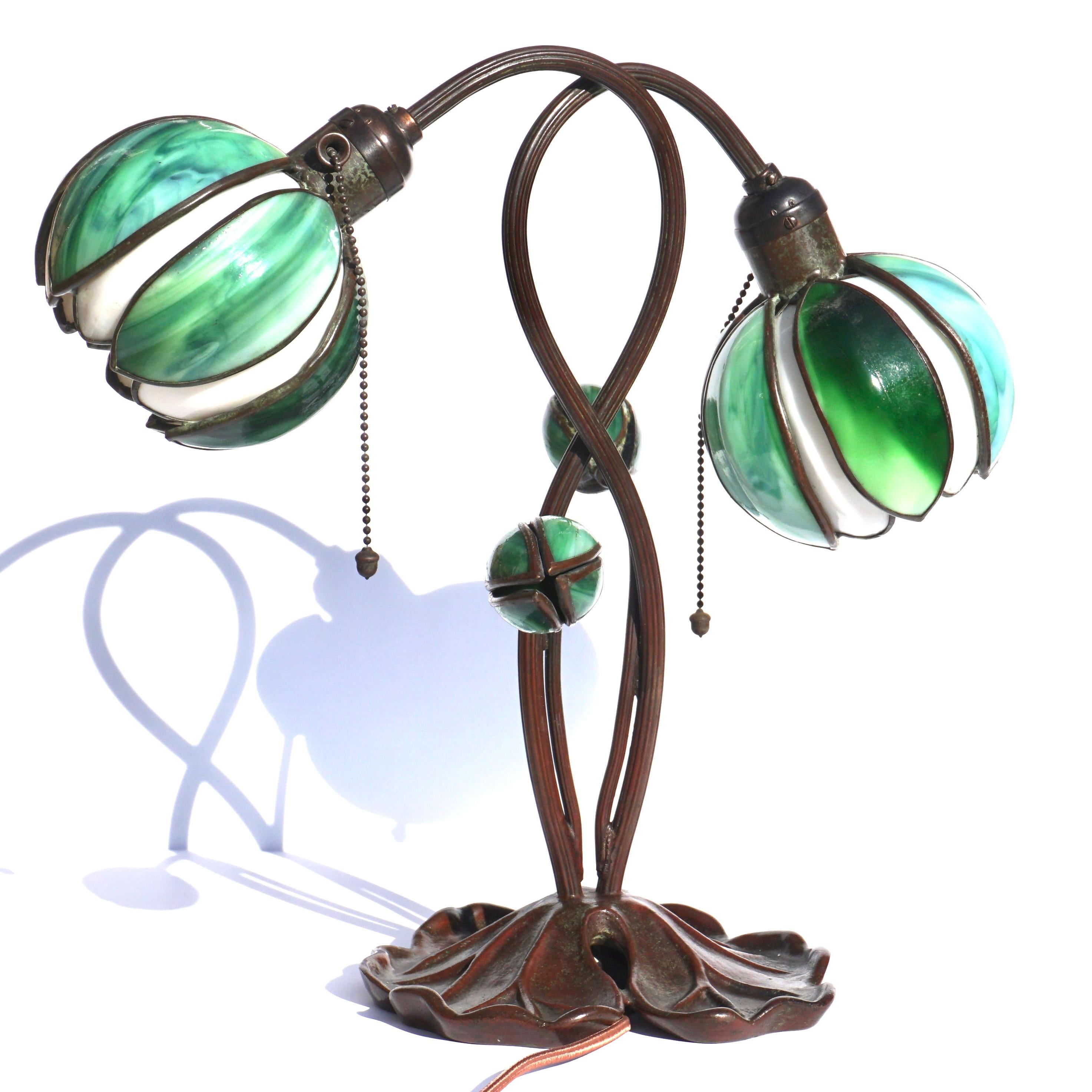 Handel Art Nouveau Zwei Licht Lily Tischlampe.

Eine schöne zweiflammige Seerosenlampe von Händel aus dem frühen 20. Die beiden Seerosenschirme bestehen aus weißen und grünen Schlackenglasblättern. Die Lampe ist außerdem mit zwei Blütenknospen aus
