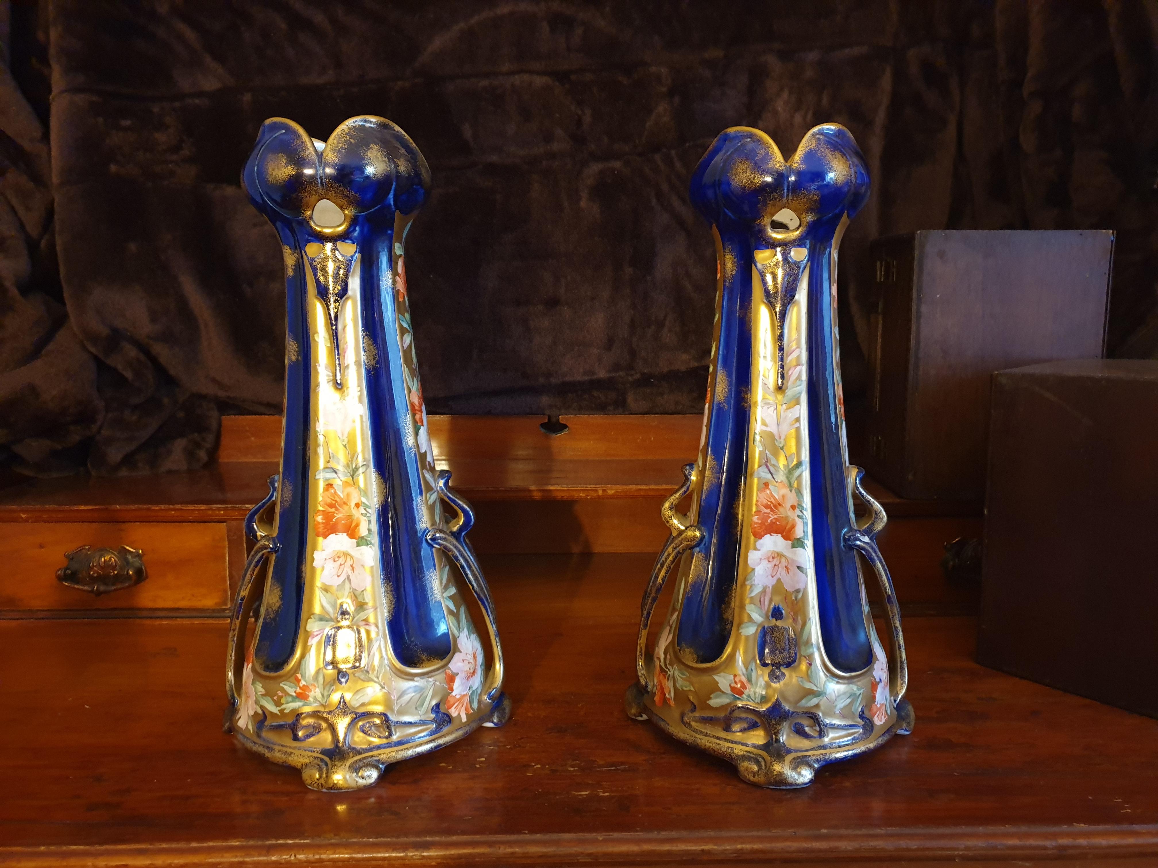 A pair of Art Nouveau English manufactured, cobalt blue ground and hand painted flowers scrolling up the side paneling. An assortment of flowers and roses with heavy 24-karat gold gilding finish all around the vase including the rounded quatrefoil