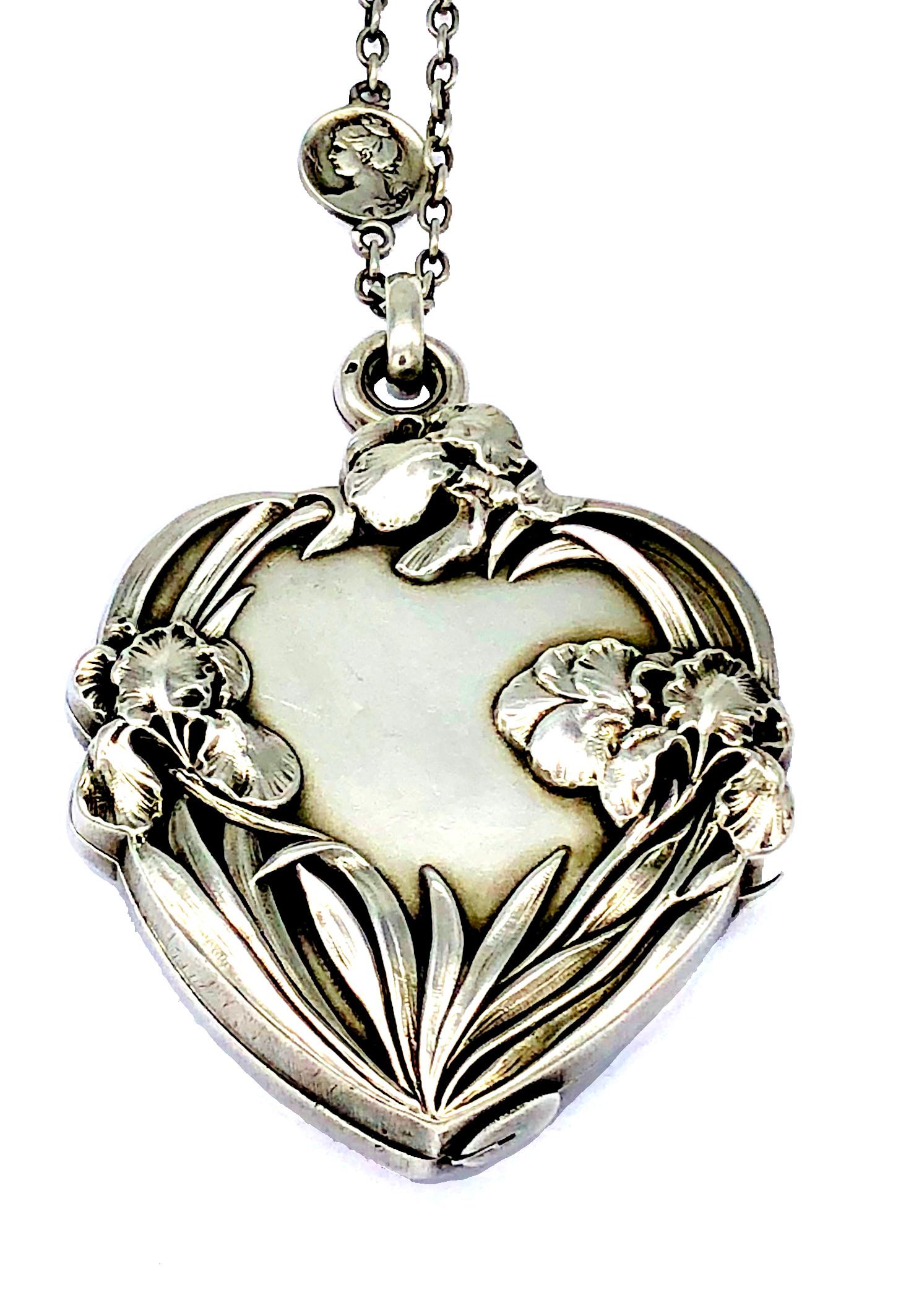This beautiful large Art Nouveau sliding silver heart shaped locket shows a young beauty amongst irises. The locket is suspended from a silver train which is interspersed with four small round medallions. Two of the medallions on one side are