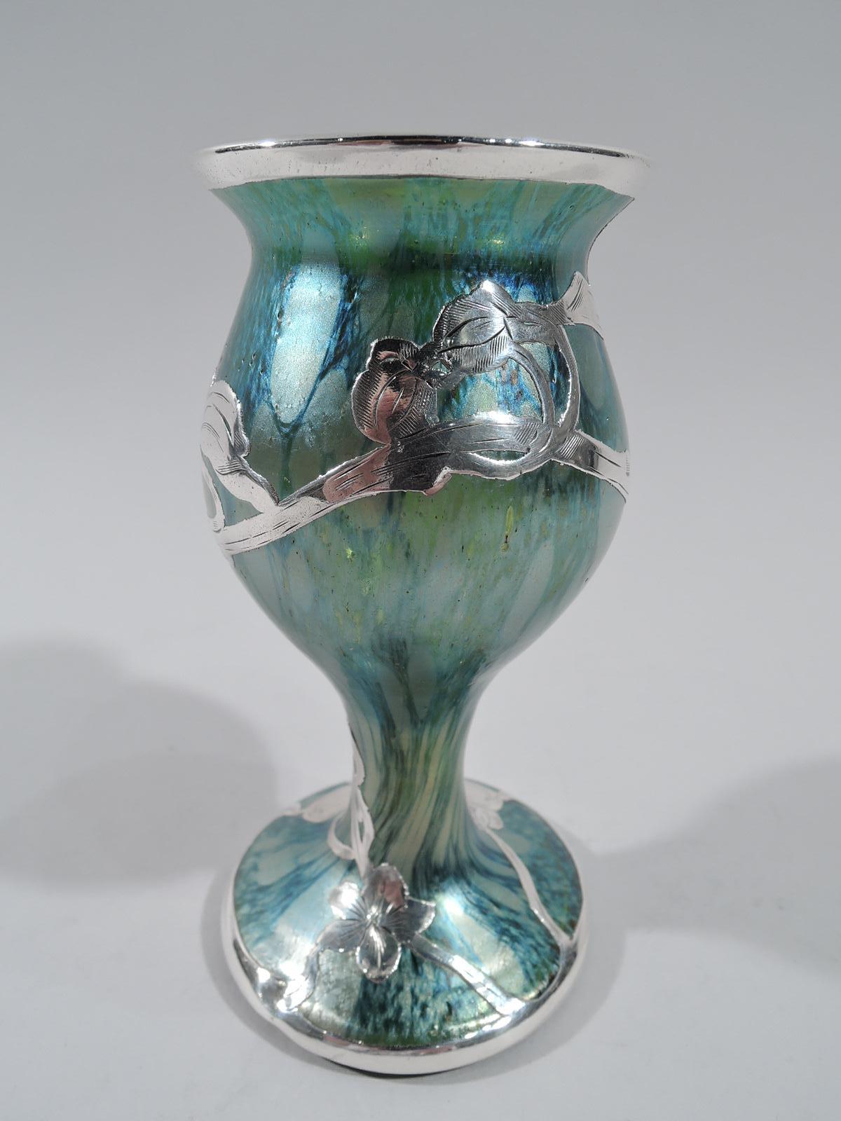 Turn-of-the-century Art Nouveau glass vase with engraved silver overlay. Baluster with flared rim and round foot. Open overlay in form of blossoming branch that encircles body and wraps around foot; tubular cartouche (vacant). Glass iridescent green