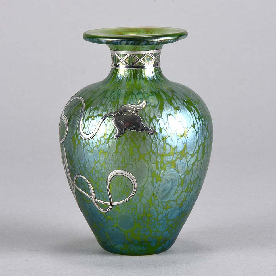 Very pretty Art Nouveau green glass vase of globular form with fine petrol blue iridescent surface and further applied with silver floral decoration to the body and geometric silver pattern to the neck.