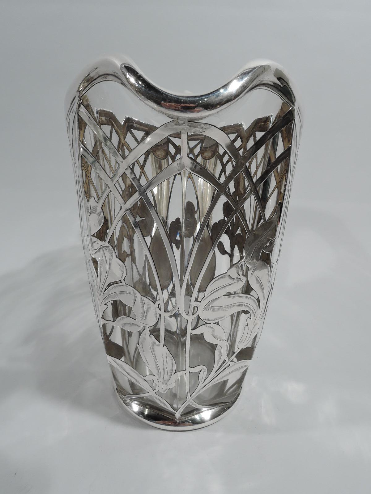 Large glass turn-of-the-century American Art Nouveau water pitcher with engraved silver overlay. Faceted clear glass body with asymmetrical and castellated helmet mouth. Silver overlay in form of trellis arcade inset with loose and fluid irises.