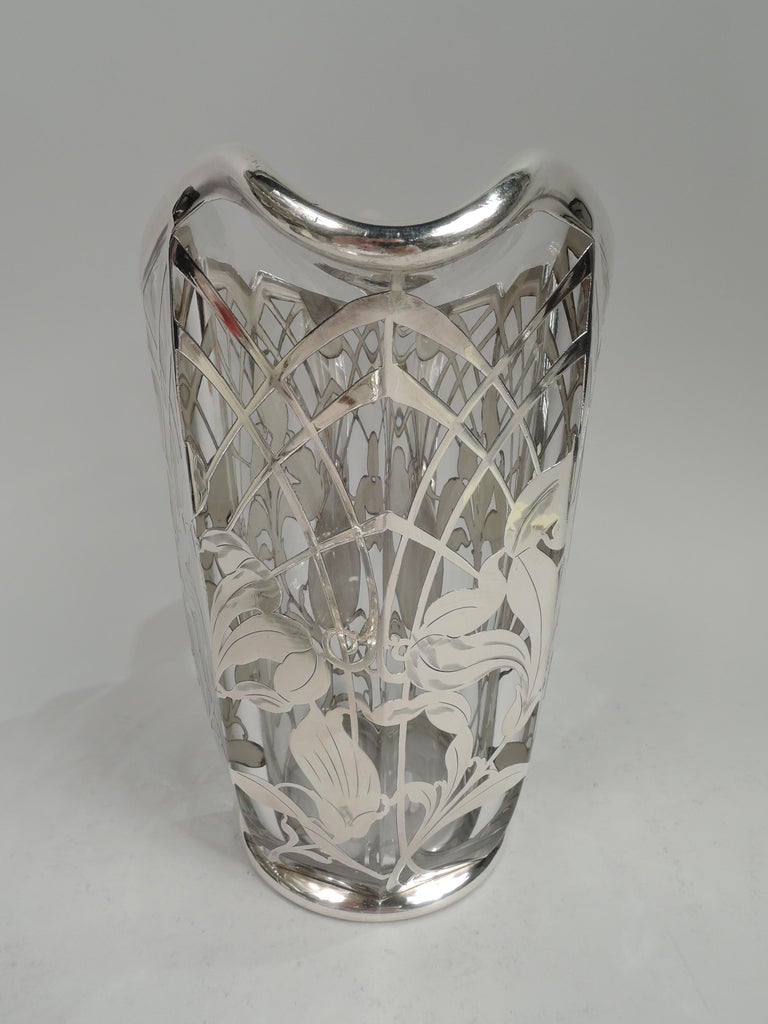 Large turn-of-the-century Art Nouveau glass water pitcher with engraved silver overlay. Faceted glass body with asymmetrical and castellated helmet mouth. Silver overlay in form of trellis arcade inset with loose and fluid irises. Scroll handle in