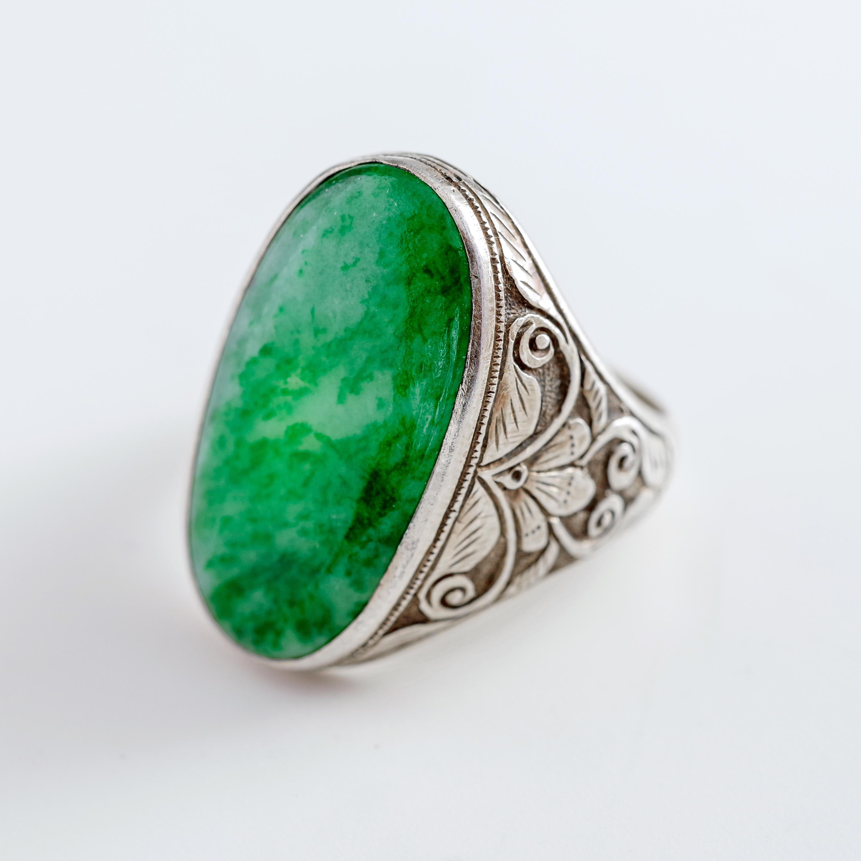 A large (24 mm x 12.5 mm) oblong vivid cabochon of certified natural and untreated jadeite jade from Burma meets its near match in an elaborately tooled yet utterly sleek silver setting, handcrafted with consummate skill and impeccable taste,