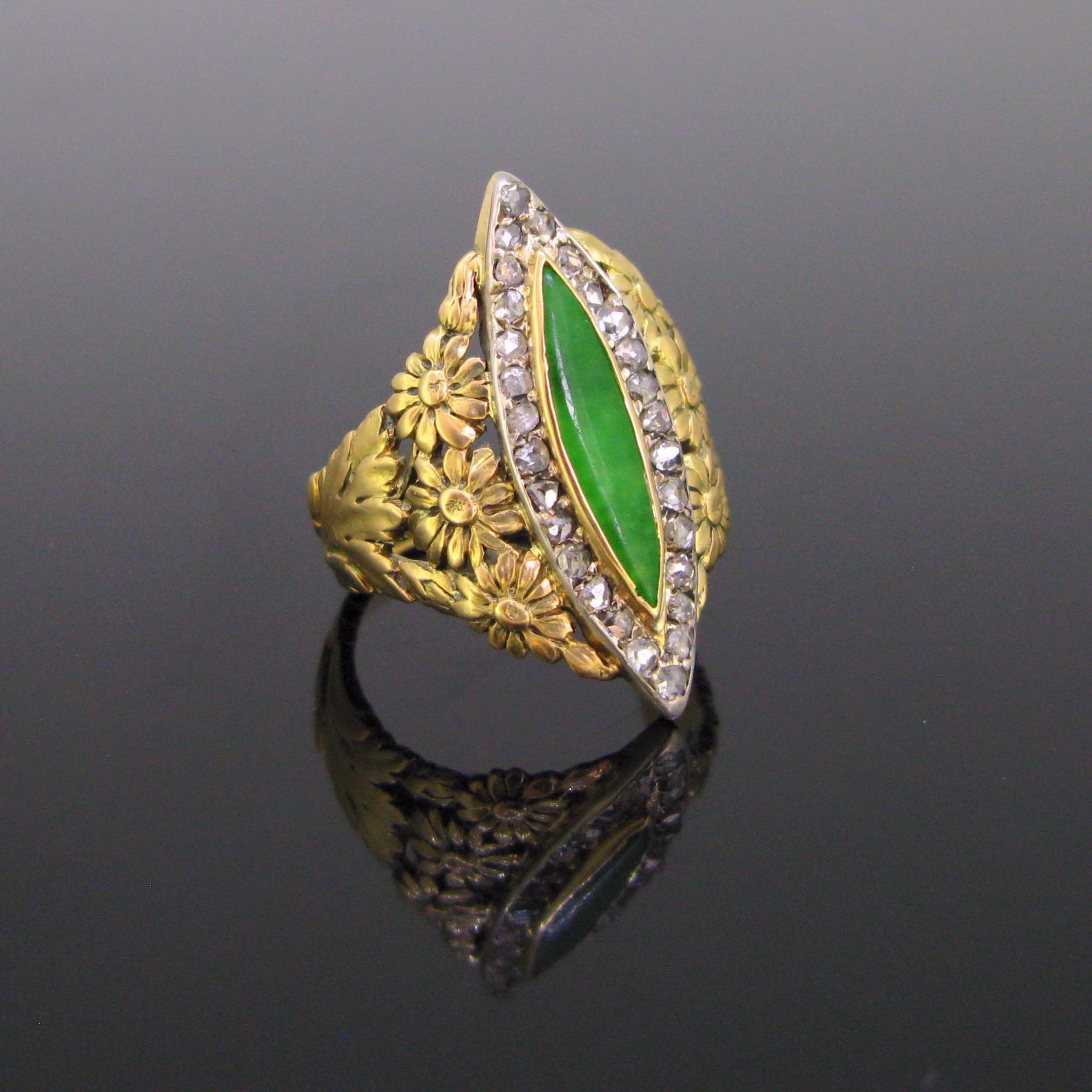 This beautiful ring is from the Art Nouveau period. It is adorned with a jadeite jade in its centre, surrounded with 28 rose cut diamonds. The shoulders of the ring have been nicely cut out into gold with flowers and leaves motifs. The diamonds are