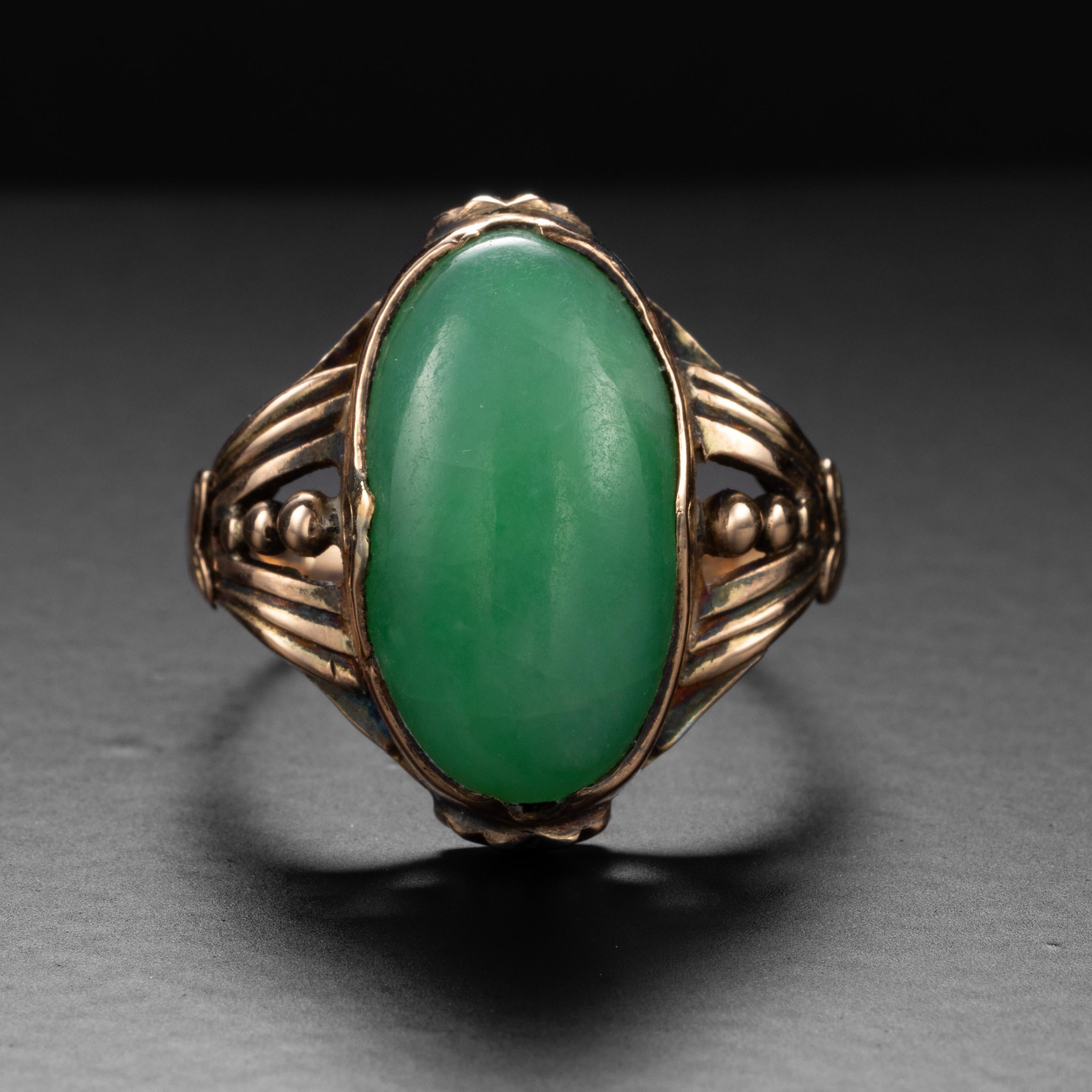 A plump oval double cabochon of bright apple green jadeite has been artfully set into a beautifully hand-fabricated 14K rose gold ring from just after the turn of the century (circa 1910). The detailing on this ring is sublime, and the jade retains