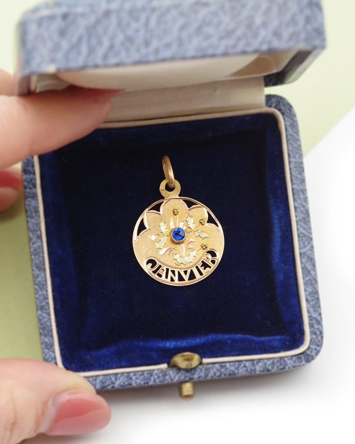 Medalla Art Nouveau del mes de enero en oro de 18 quilates. Un precioso colgante de aniversario de enero decorado con hojas de acebo y adornado en el centro con una piedra de imitación de cristal azul. El mes de 