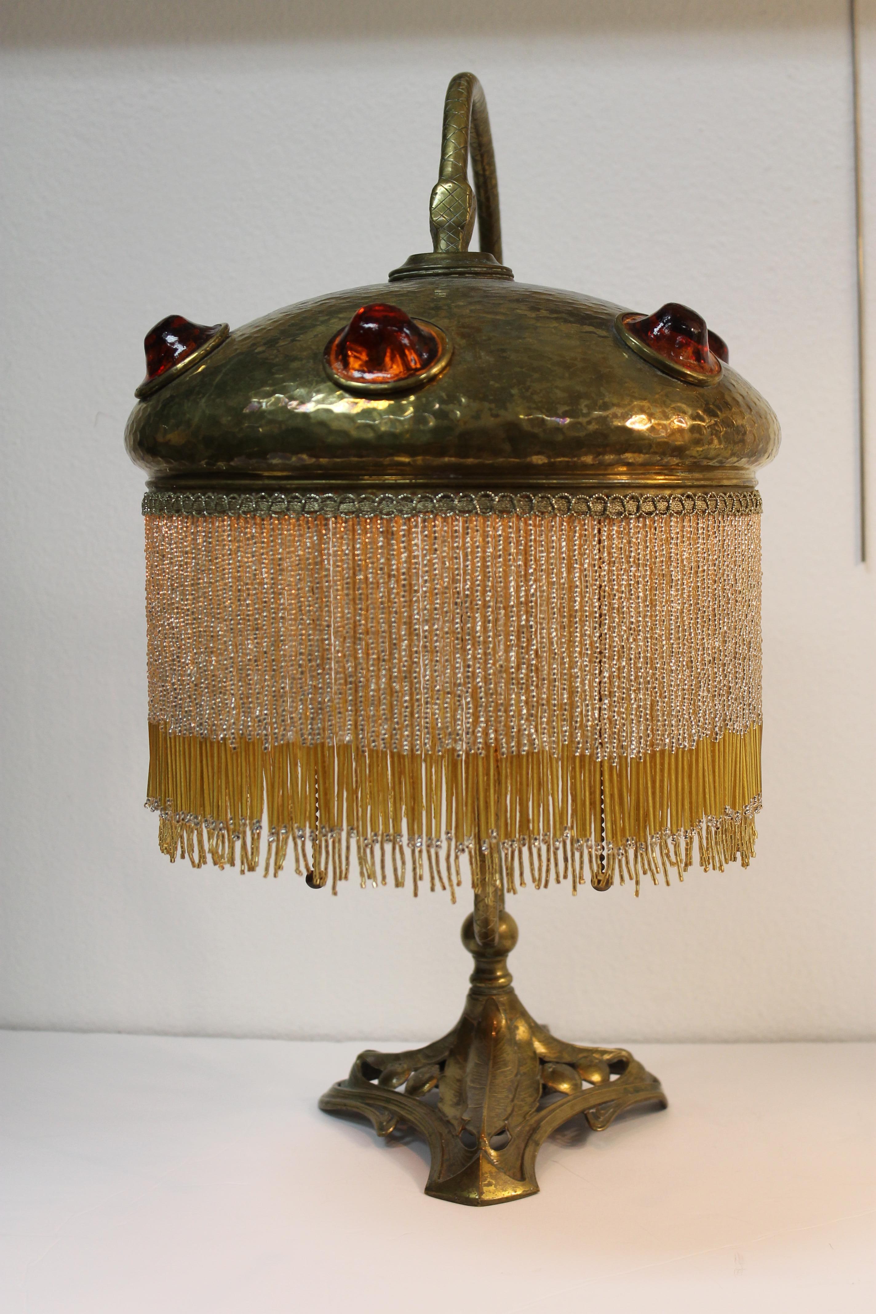 An early 20th century solid brass lamp with a coiled snake or serpent holding the shade. Shade is set with large amber nuggets of glass. Measurements are 20.5