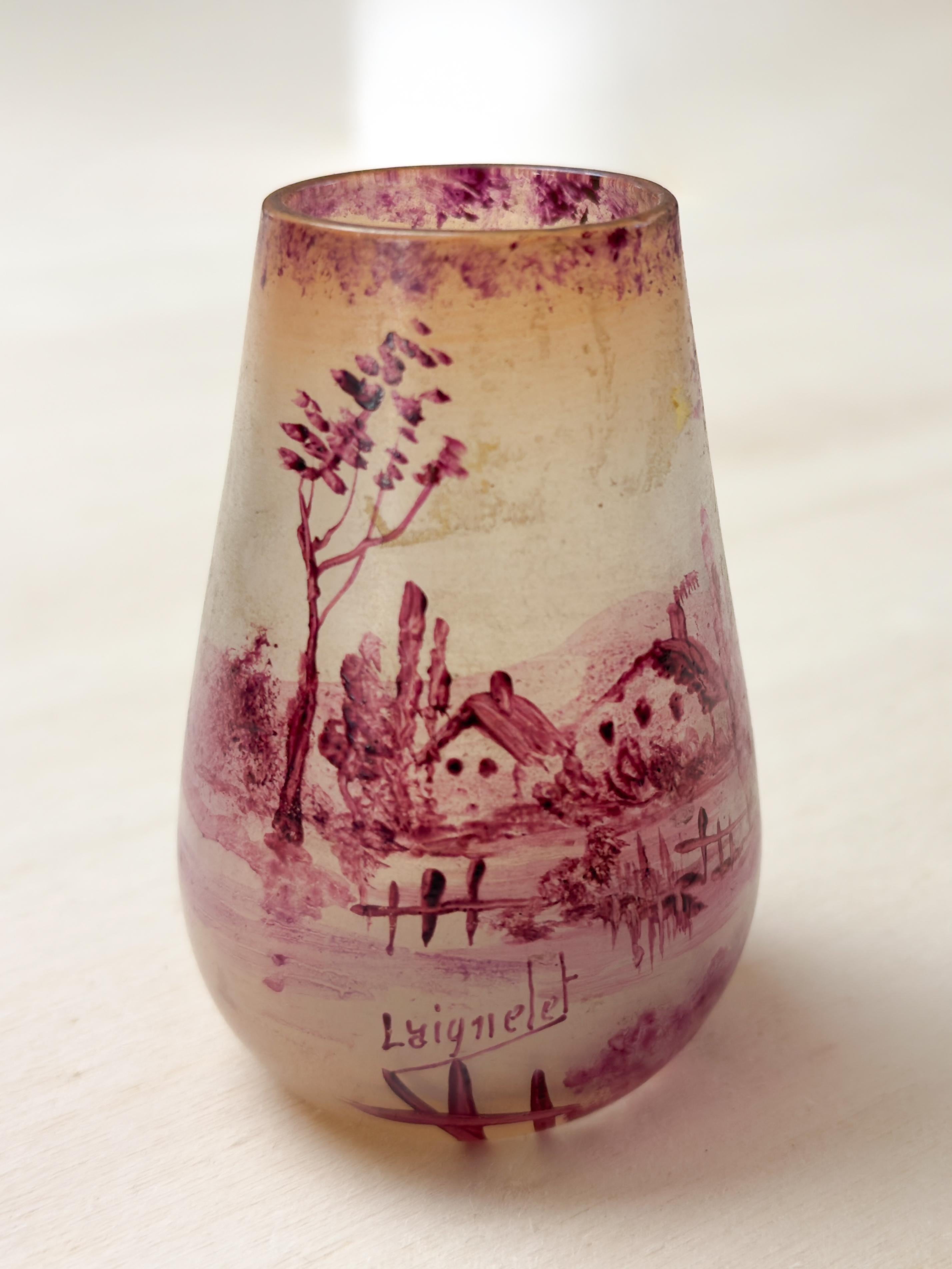 Pequeño y encantador jarrón de cristal Art Nouveau de la Verrerie de Laignelet, con una escena panorámica de la región de Bretaña pintada al frío en un delicado color rosa. 
El jarrón está decorado con las características casas bretonas, ofreciendo