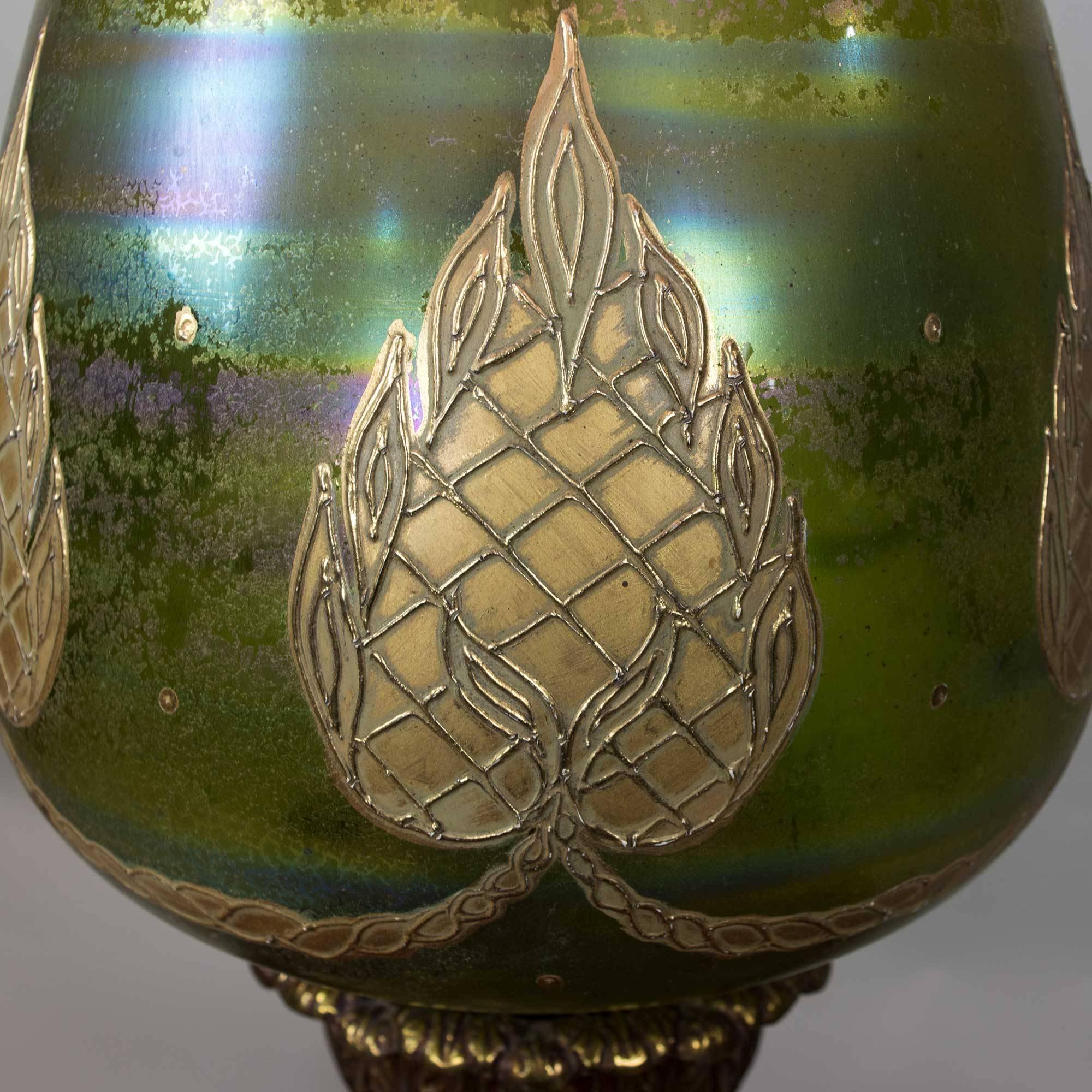 Eye-catching extra-large green glass table lamp with gorgeous hand-painted design in an aged gold tone and additional subtle colors including blues and purples. Additional details include the square base with an aged treatment in a dark metal tone