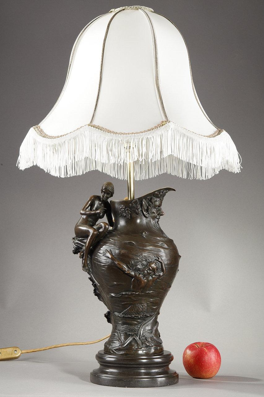 Art Nouveau lamp mounted on a sculpted and chased bronze vase, signed A. Clerget. This lamp carved in relief, presents a seated woman forming a handle, a head of sylvan among vine leaves and grapes winding a spout. The shaft of this 1900 light