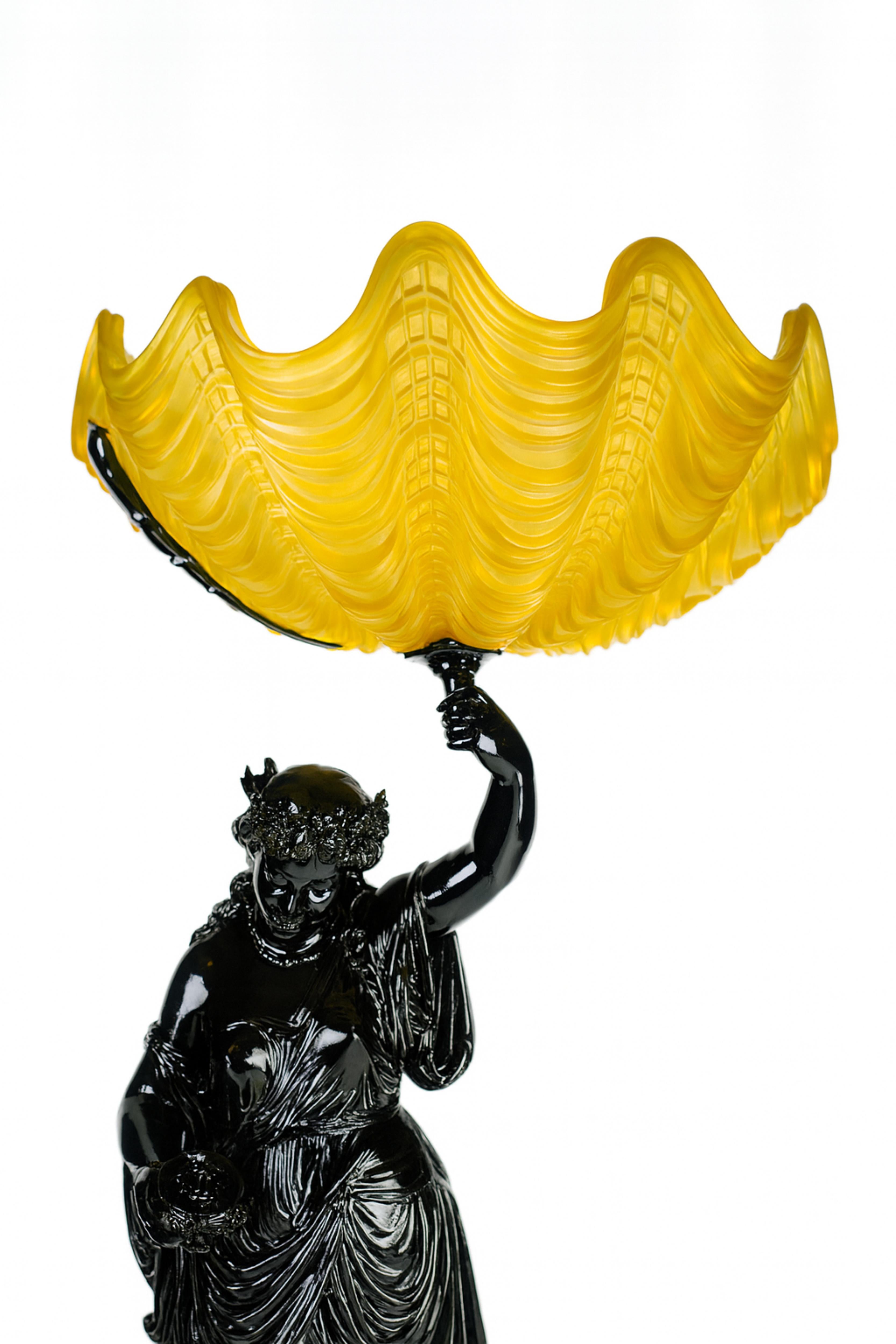 Lampe-sculpture Art Nouveau en métal laqué noir refini, représentant une gracieuse femme de la Belle Époque tenant un bol en verre d'un jaune éclatant,
La sculpture représente une jeune femme sereine, parée d'une draperie fluide et d'une couronne de