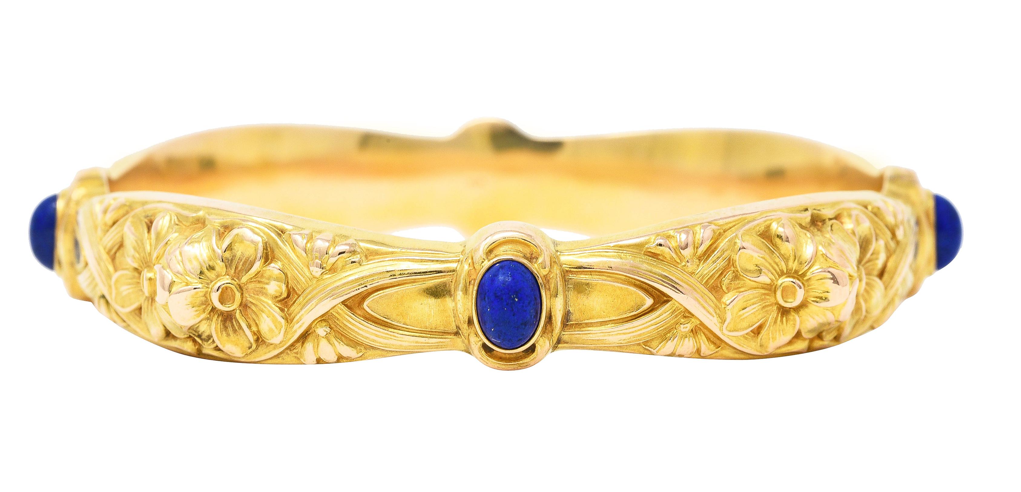 Designed as a bangle bracelet with a highly rendered repoussé woven daisy motif. Featuring four oval stations centering bezel set lapis lazuli cabochons. Measuring 5.0 x 7.0 mm - opaque ultramarine blue with pyrite flecking. Stamped for 14 karat