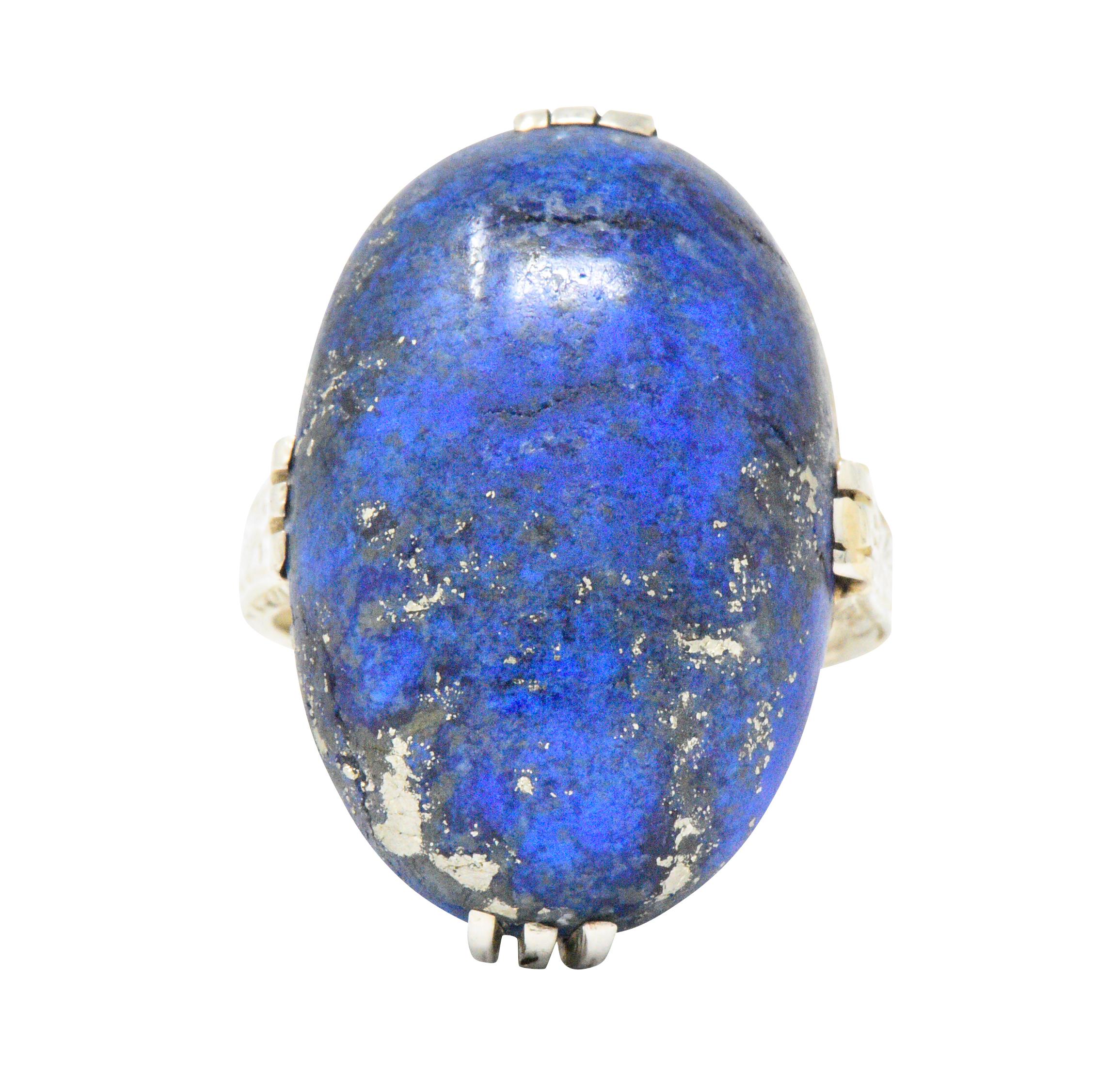 Centering an oval cabochon lapis lazuli measuring approximately 23.0 x 15.0 x 6.0 mm

Bright deep blue with flecks of pyrite

North, east, south, west trip-split prong setting with lovely engraving detail around and part-way down the shank

Fun bold