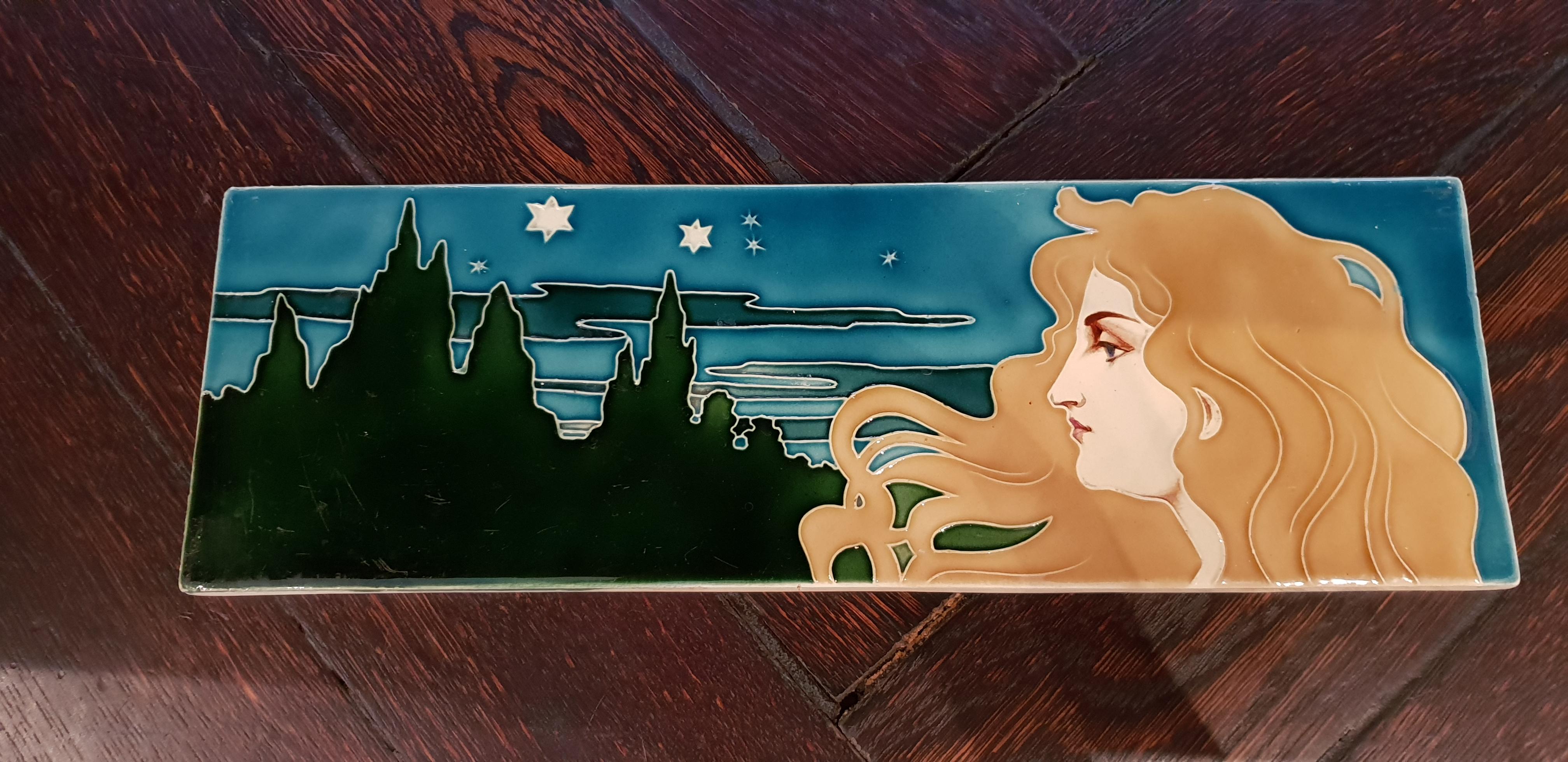 Art Nouveau ceramic tile, circa 1900. Designed by Carl Sigmund Luber (1896-1934), Germany. Manufactured by Johann von Schwarz, Nuremberg. Stoneware, glazed. The maid face is hand-painted. Numbered on the back: R 663.
Dimensions: 4.72 x 14.17 x 0.39
