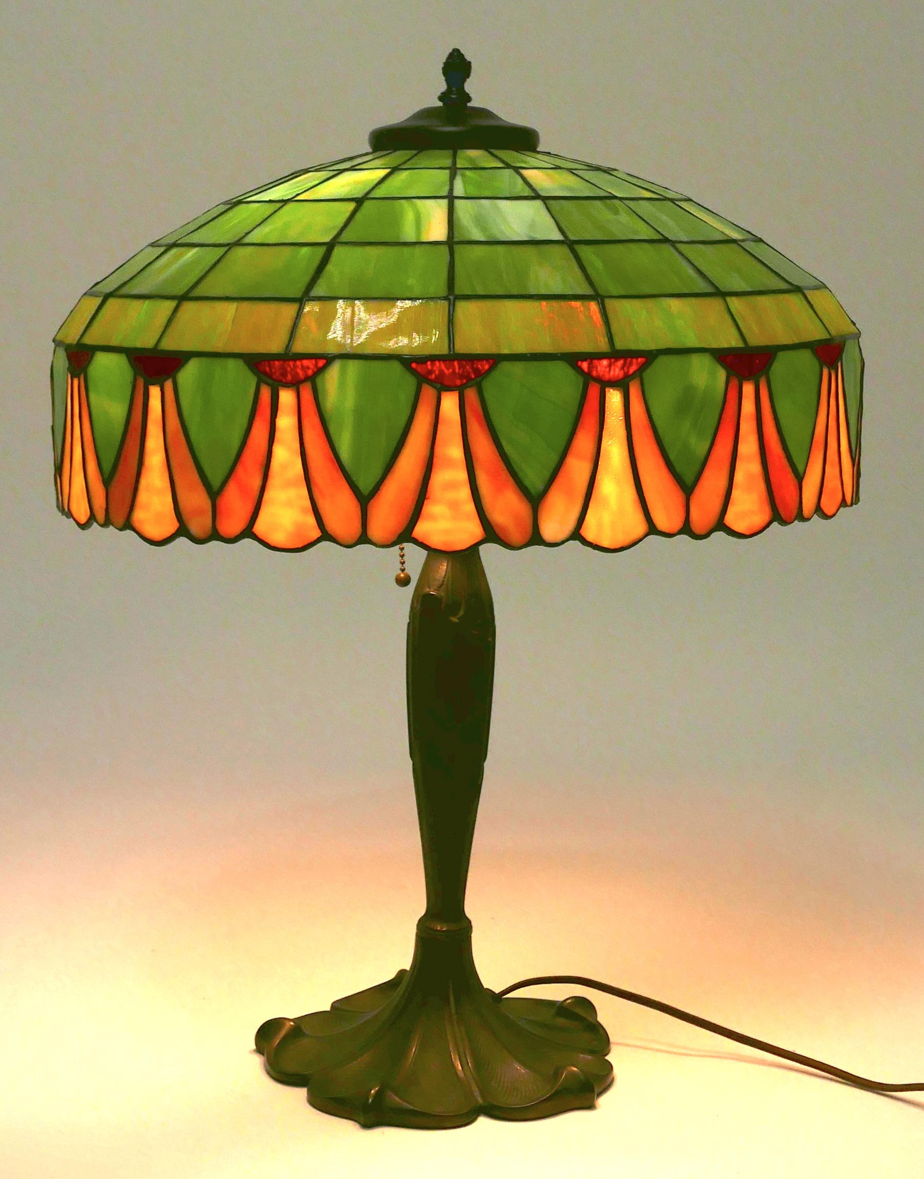A fine Art Nouveau period leaded glass shade and a graceful brass plated cast iron base table lamp by the Indiana firm: Lamb Bros. & Greene. In the manner of Tiffany Studios.
American, circa 1910- 1920.