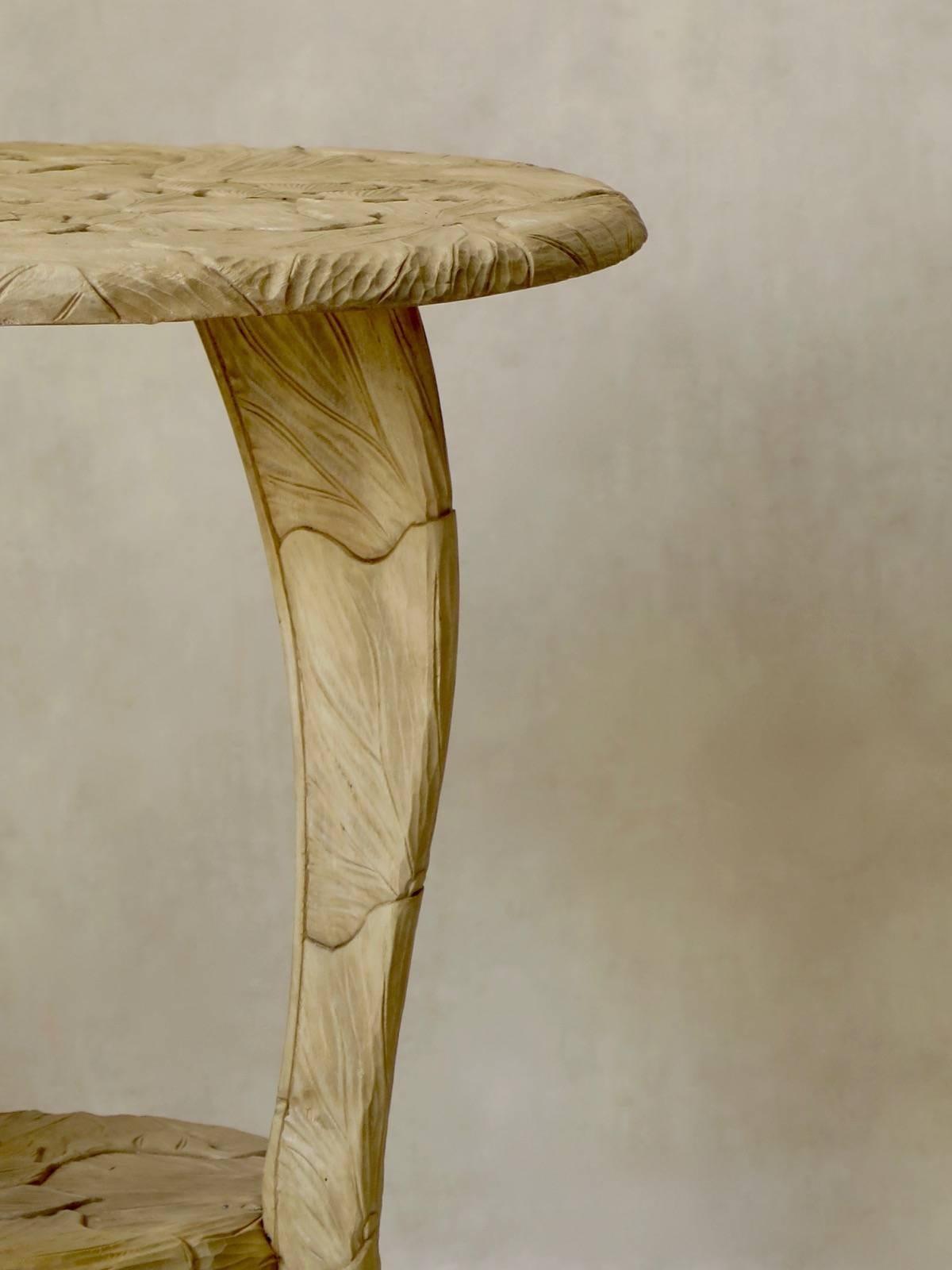 Two-tier circular tripod bleached beechwood table, extensively carved with large, exotic looking flowers.