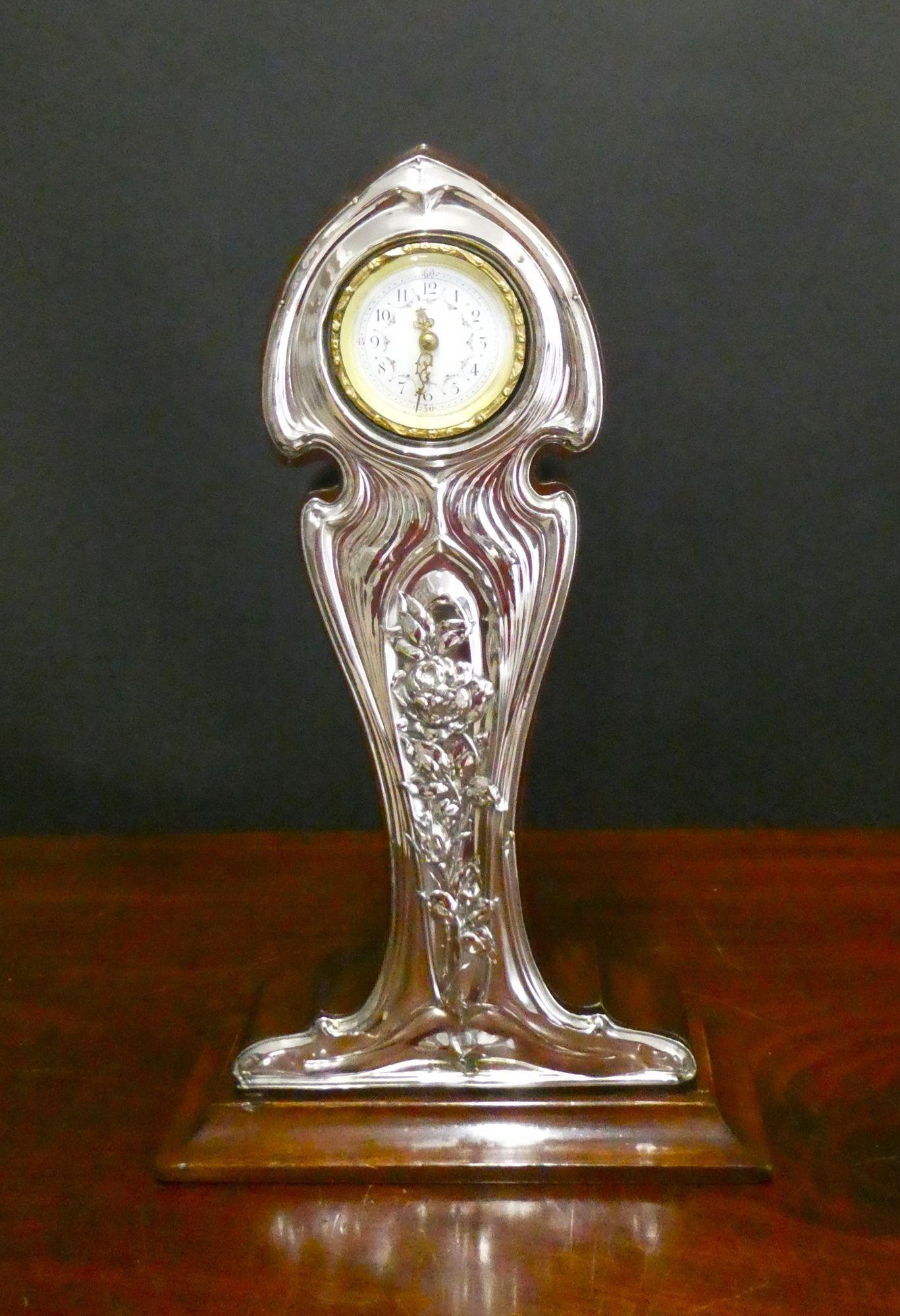 Art Nouveau Mahogany and Silver Mantel Clock
A rare Art Nouveau mantel clock housed in a waisted mahogany case with applied silver front and standing on a stepped base. The silver front decorated with scrolls and floral decoration and bearing the