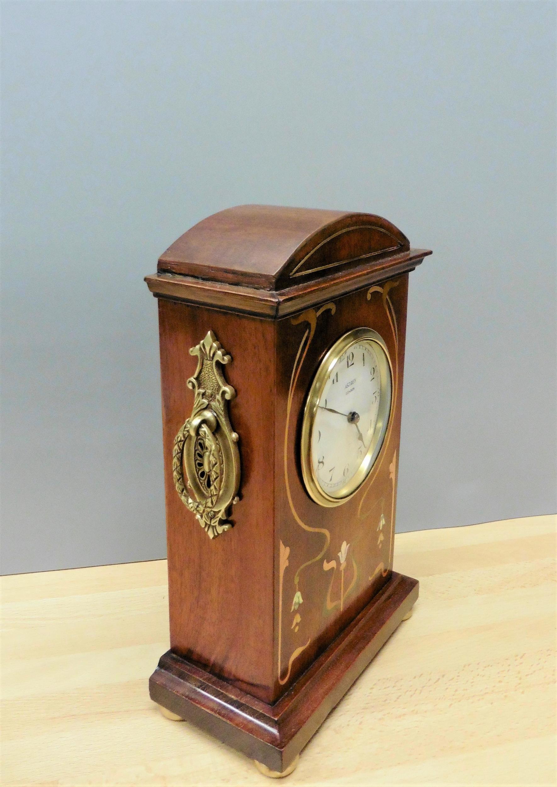 Art Nouveau mahogany mantel clock

Mahogany cased mantel clock with arch top, brass side carrying handles and satinwood and mother of pearl stringing and floral inlay standing on a stepped moulded plinth and resting on four brass bun