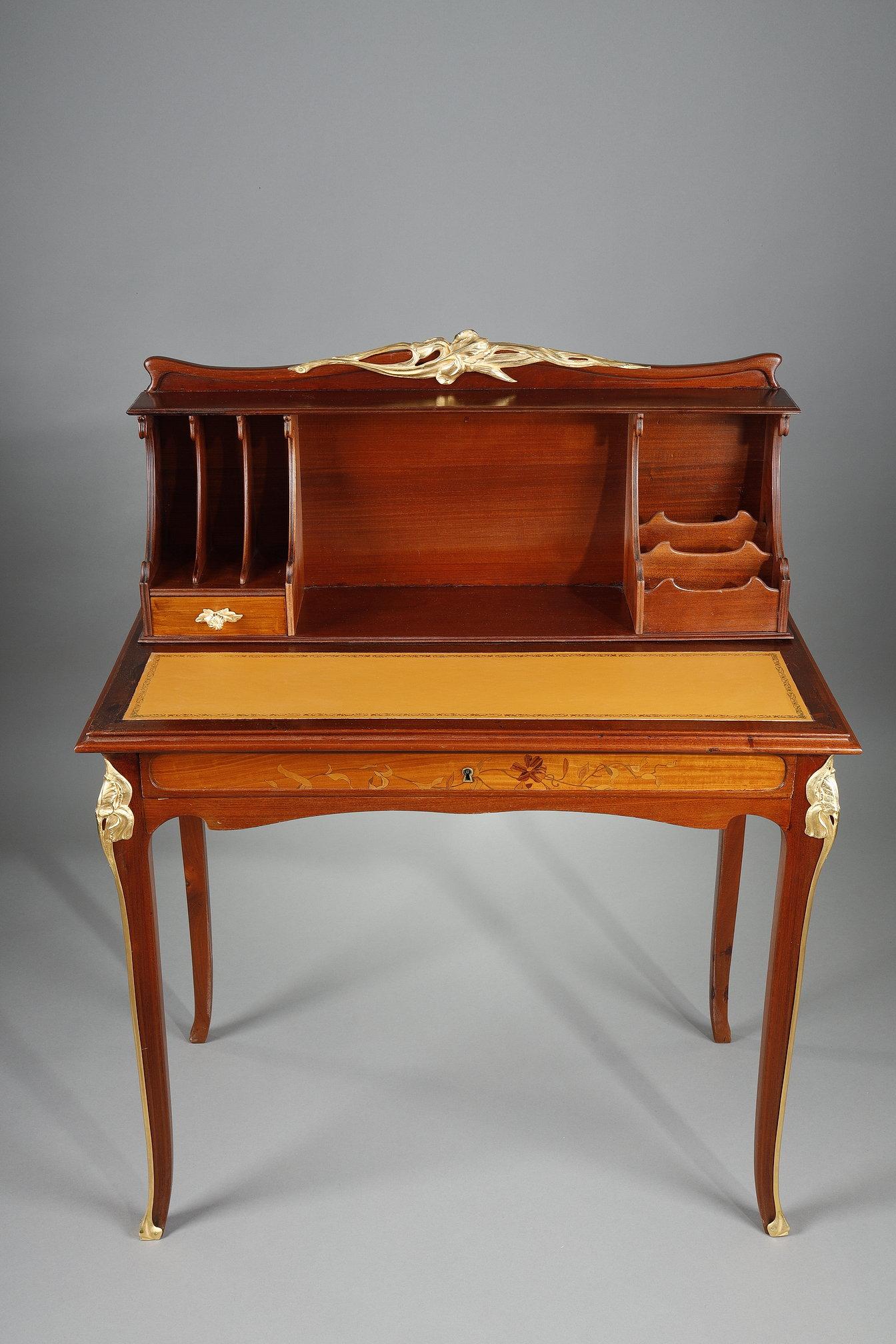 Elegant stepped desk in mahogany and mahogany veneer. Gilt bronze frame opening with a drawer inlaid with leaf and flower stems. The front features a drawer with an ormolu catch and compartments forming a courier tray. The legs and top are