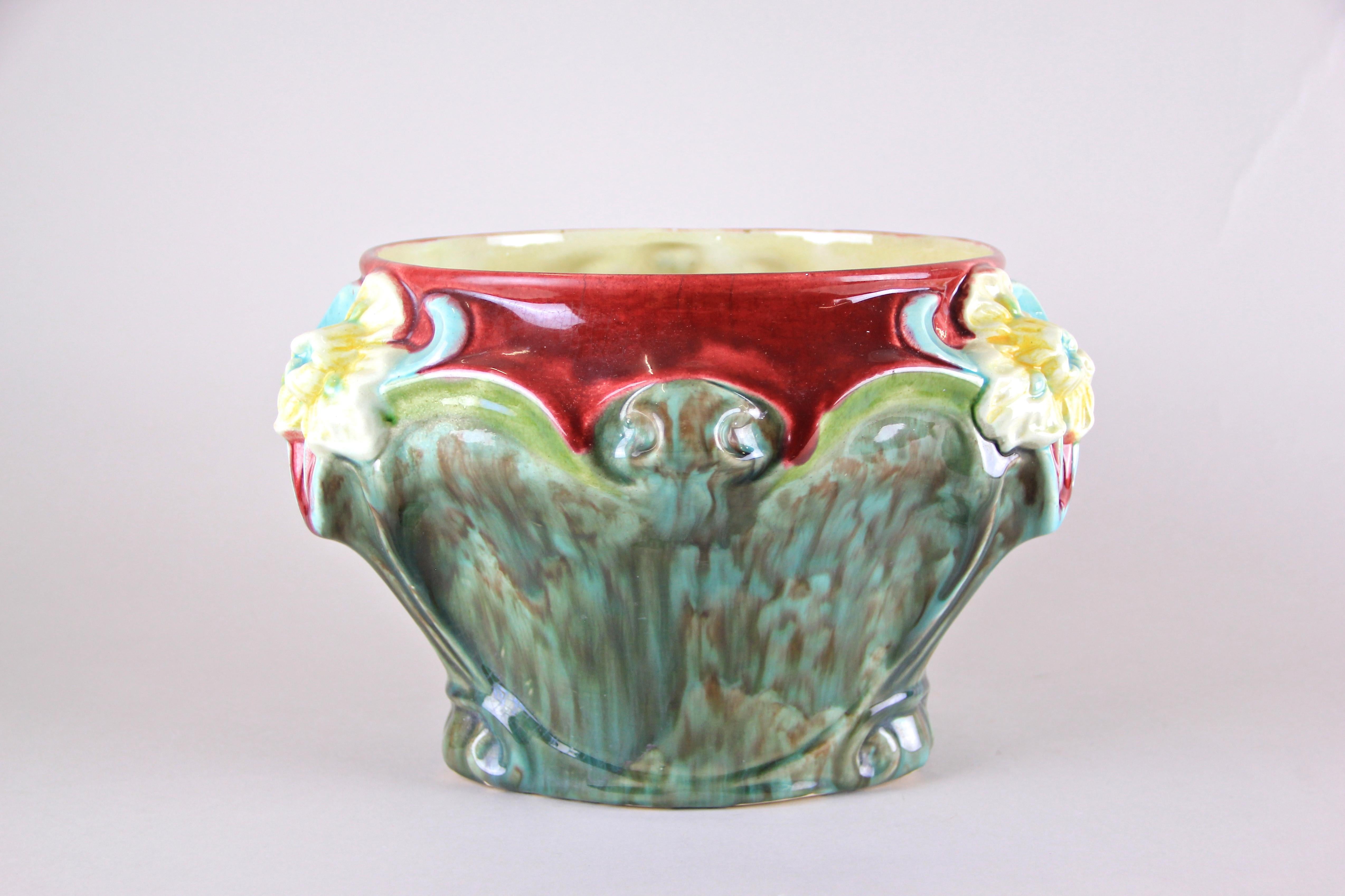 Colorful Art Nouveau Majolica cachepot from the early period in France around 1910. The lovely floral design with three big blossoms in light blue and yellow harmonizes perfectly with the unique shaped turquoise, green and red hand painted body. A