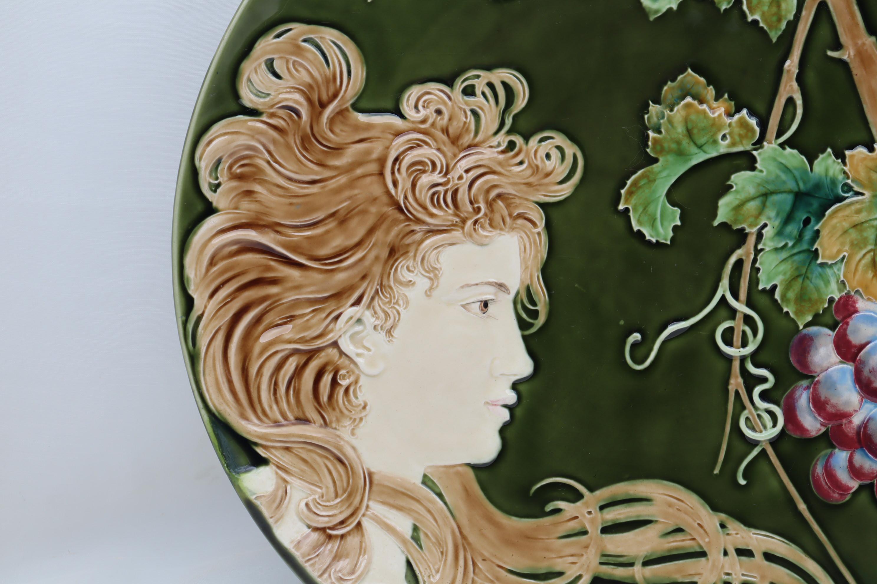 This large wall plaque is decorated with Majolica glazes to enhance the typical Art Nouveau pattern of the young girl and her long flowing tresses. The raised moulded design has been coloured by hand, and then using the sgraffito technique, small