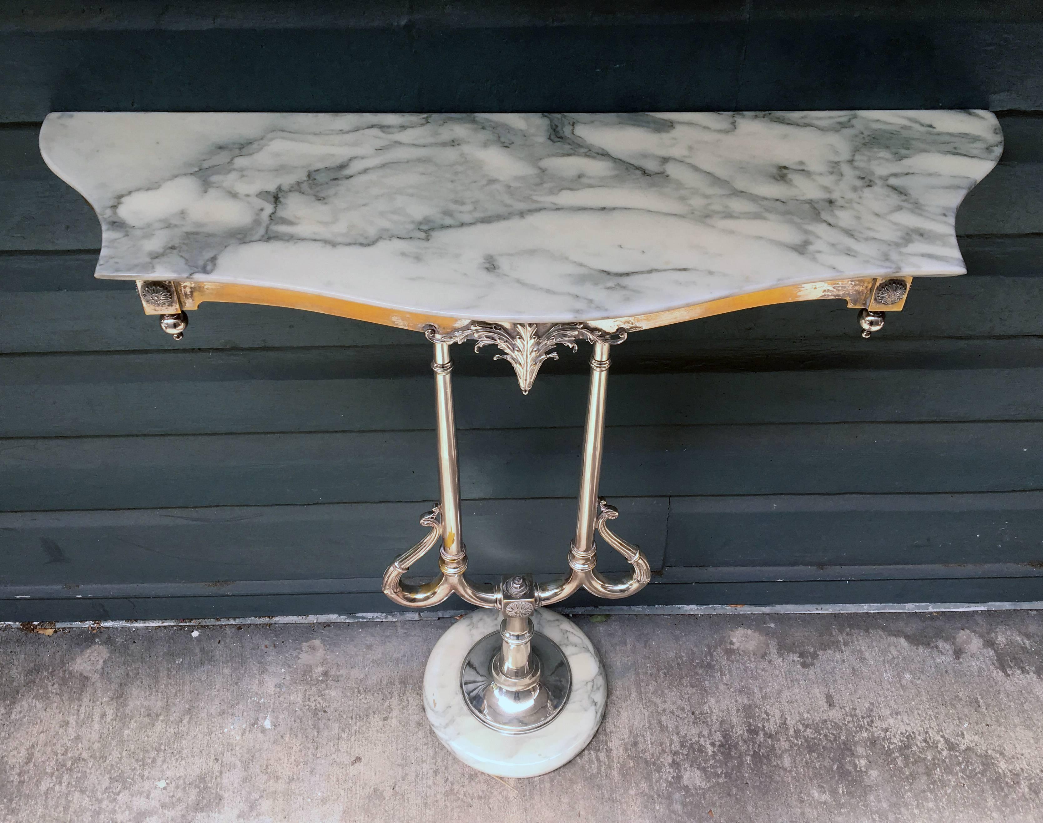 This turn of the century Art Nouveau console table has a beautiful marble top surrounded with brass and highlights of silver. This table has a silver plated over bronze lyre shaped leg.