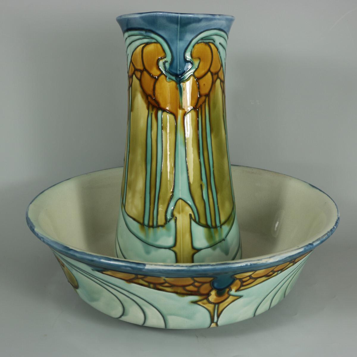 Minton Secessionist No.8 jug and wash bowl. Decorated in shades of blue, orange and green. Grey tube lined art nouveau stylized motifs. Cream interior to both. Maker's marks, including impressed 'MINTONS' mark, printed 'MINTONS LTD. No.8'. Impressed
