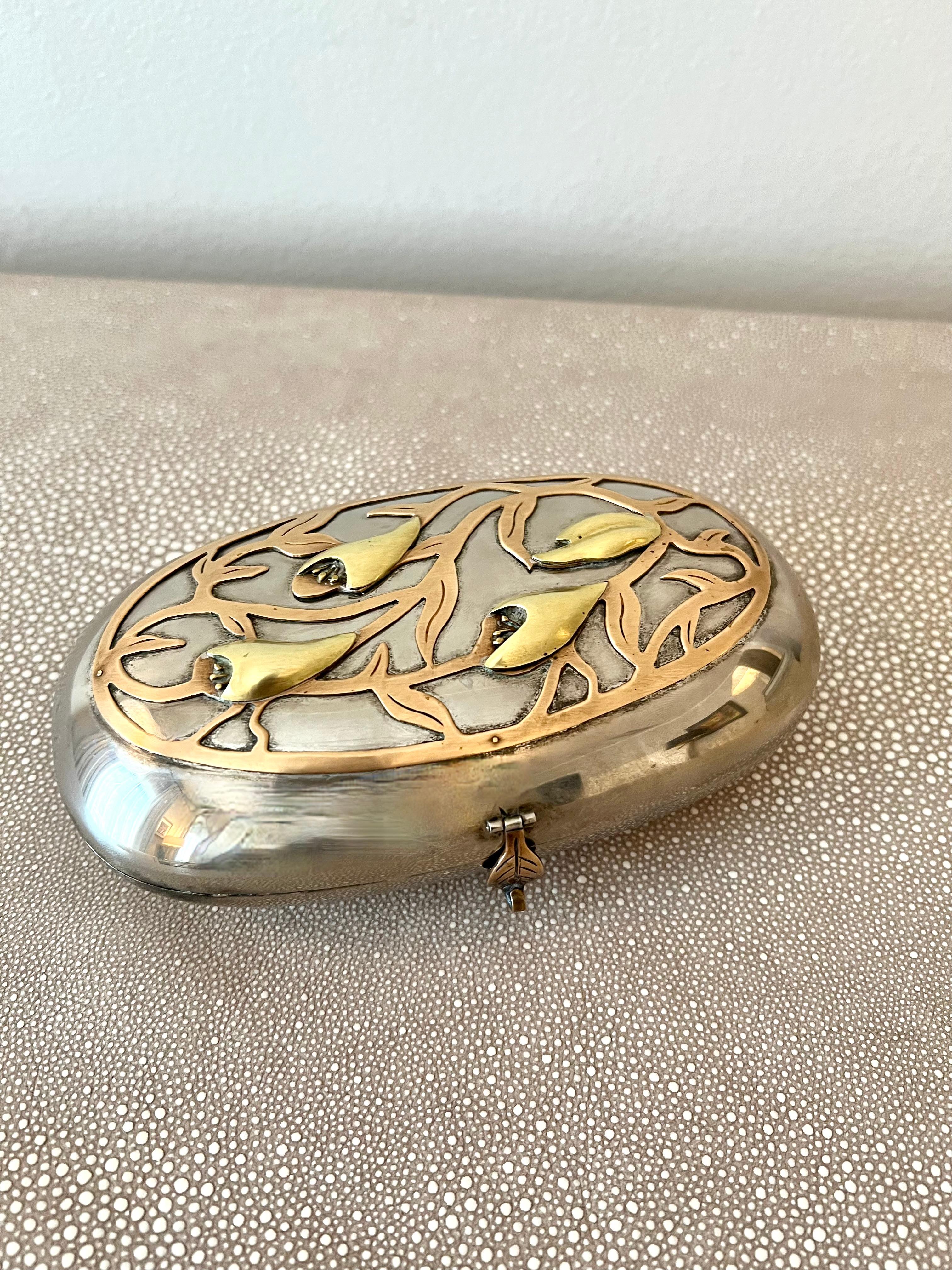 Shining art nouveau decorative box with floral detail and charming patination. 

A handmade intricate design of brass tulip-style flowers and their leaves decorates the top of this box. A brass leaf serves as the clasp-style closure to the black