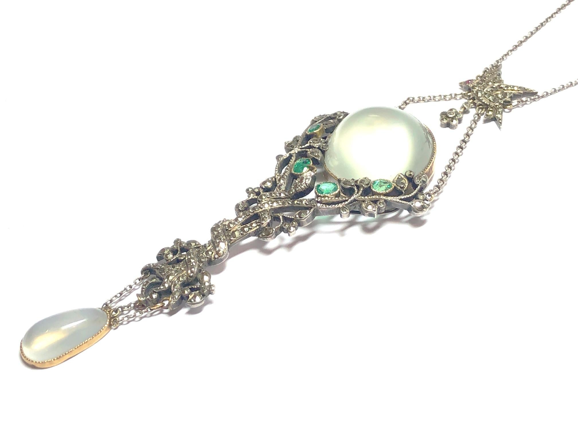 An Art Nouveau moonstone, emerald and marcasite silver mounted pendant. The circular moonstone supported set in a gold mount, set above an emerald leaved tree with serpents entwined around the trunk the base suspending a pear shaped moonstone, all