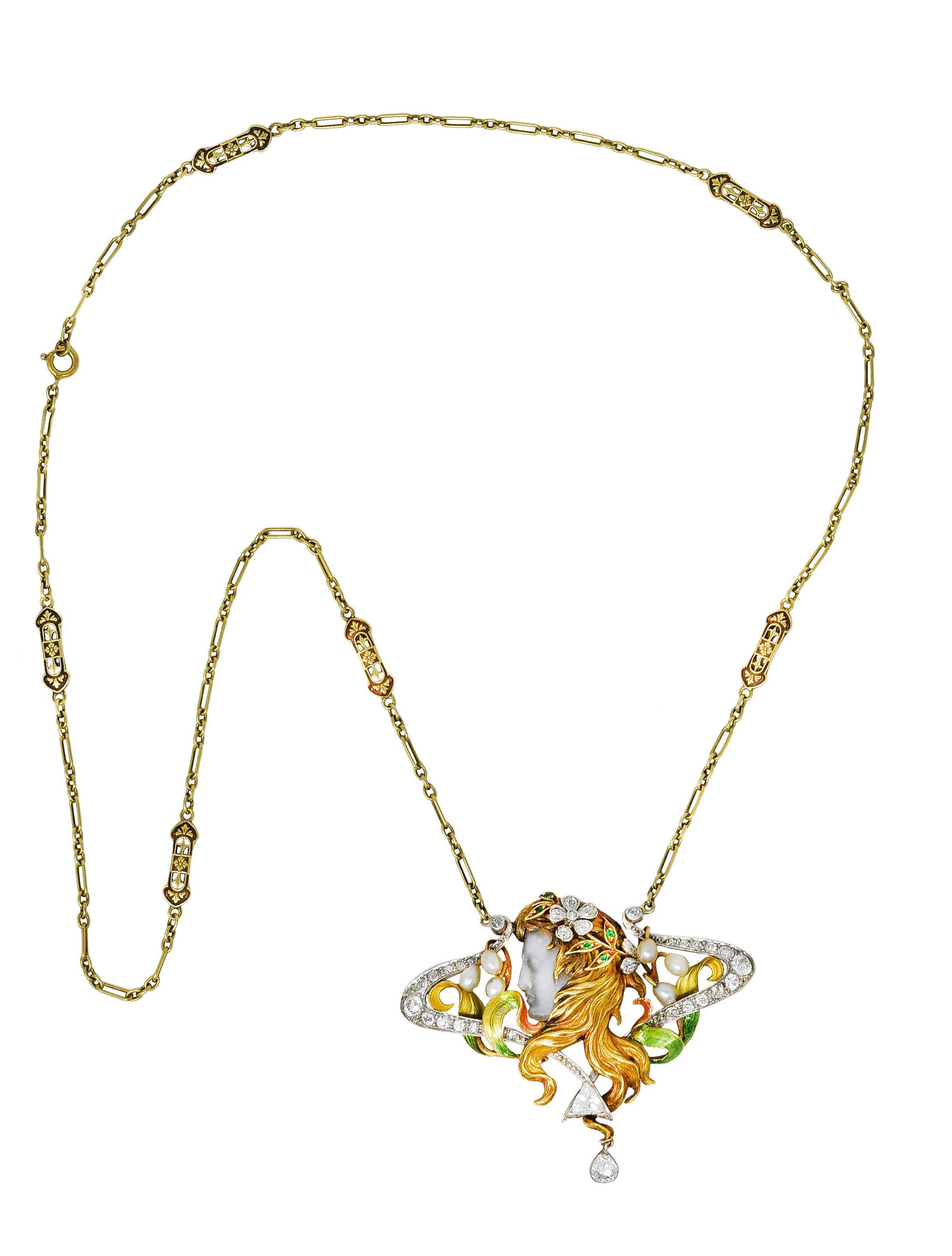 Necklace is comprised of a green gold link chain with stylized floral bar stations. Suspending a substantial whiplashed enhancer pendant via two 14 karat gold spring ring clasps. Pendant depicts a woman with texturous gold hair and scrolling