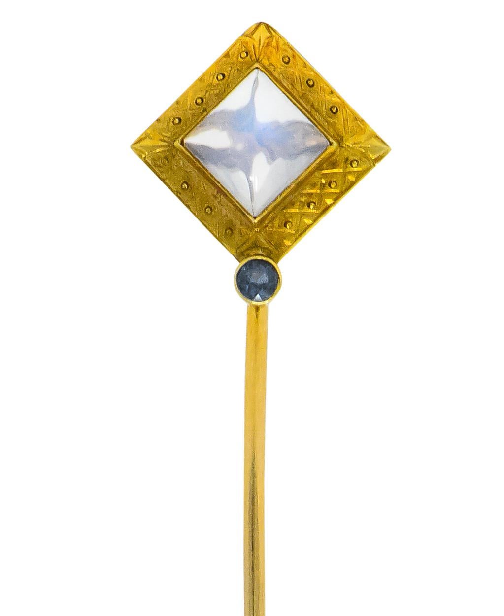 Centering a sugarloaf moonstone measuring approximately 6 x 6 mm, translucent with slight white adularescence

Bezel set in a decorative mount engraved with stylized corners, crosses, and circle motif

Accented by a bezel set, round cut sapphire,